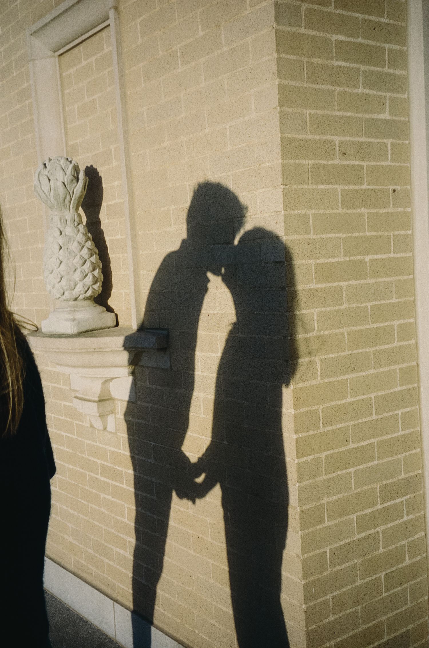 A series of shadow silhouettes on a beige brick wall show two figures interacting in progressive frames.