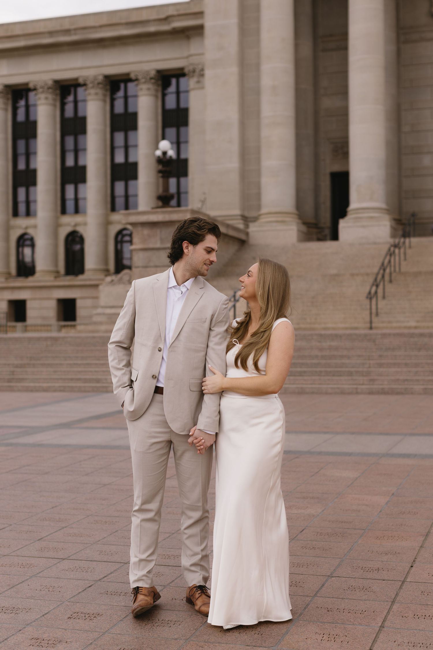 A couple poses together on a grand plaza with stone columns and steps in the background.