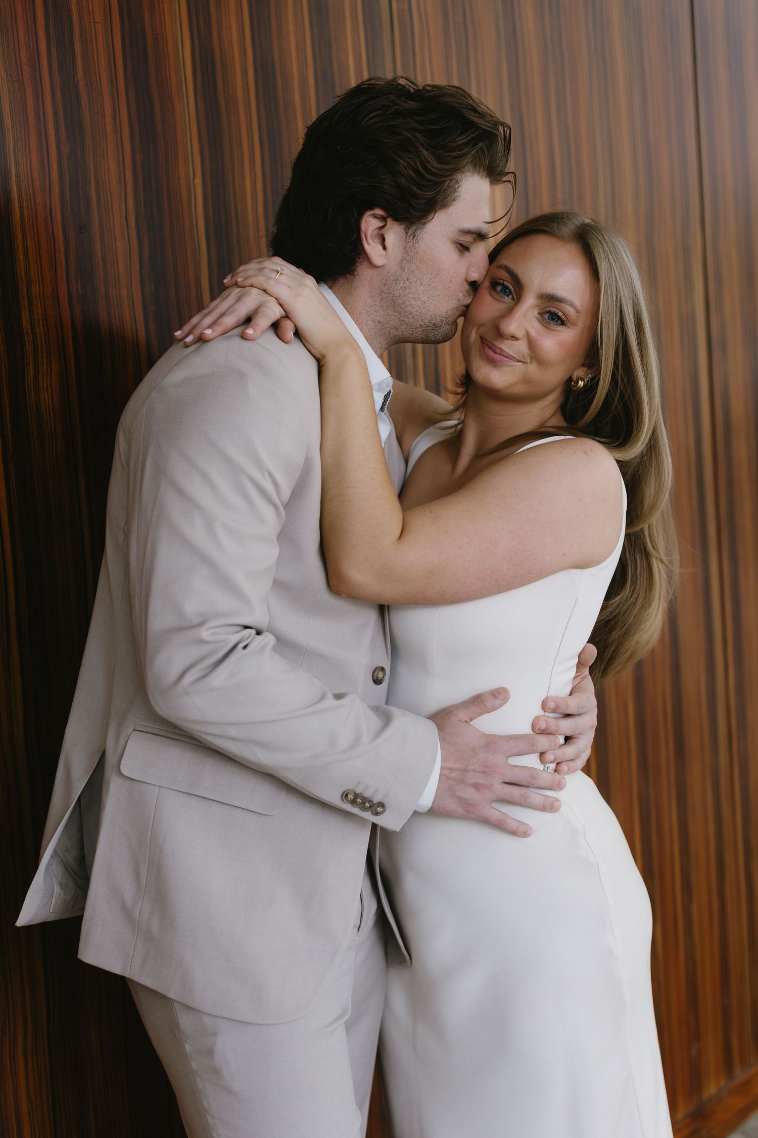 Romantic embrace of couple in white and beige clothing against dark wood paneling.