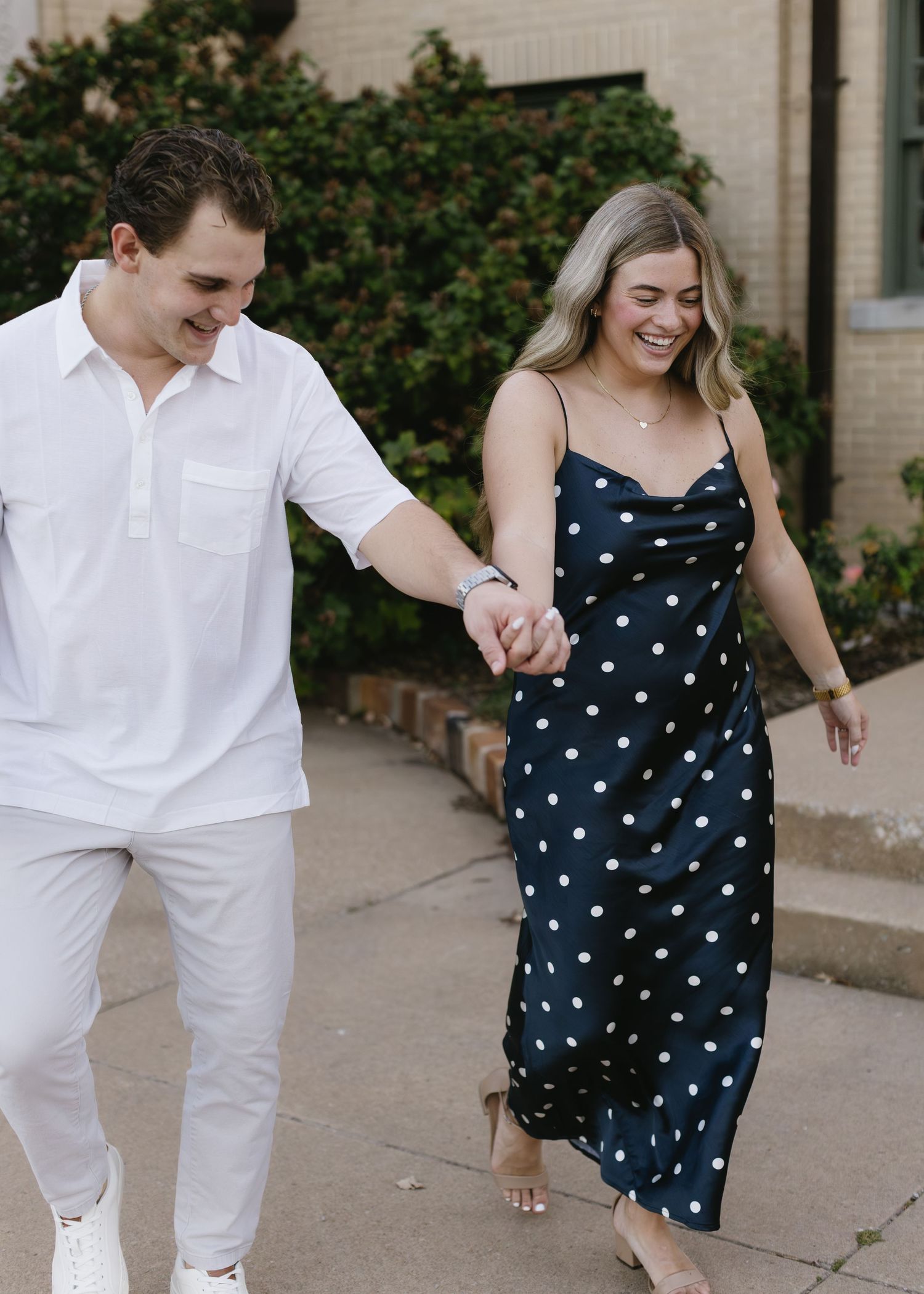 Couple walking together on sidewalk wearing coordinated white and navy polka dot outfits.