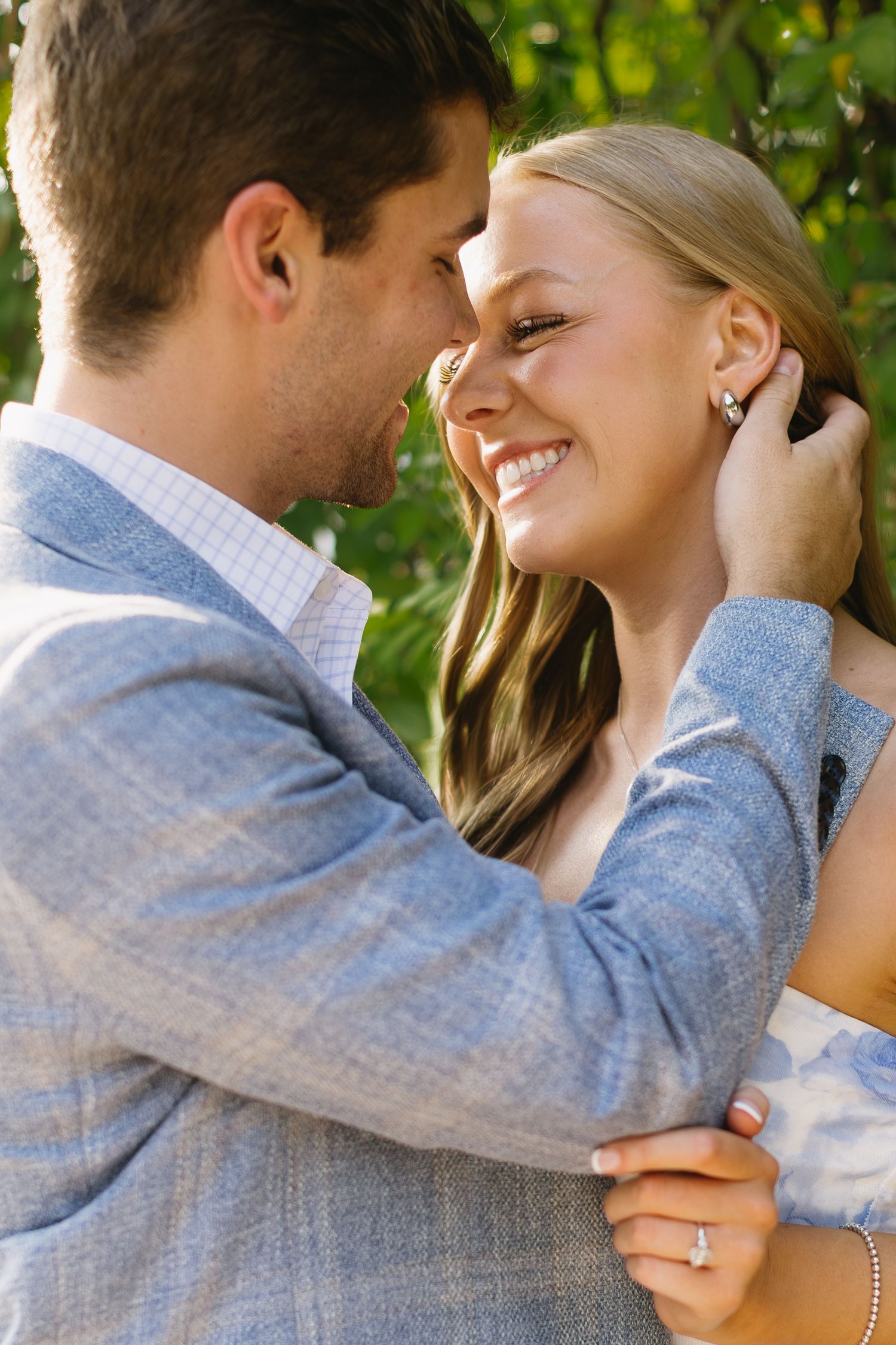 A couple shares an intimate moment outdoors with green foliage in the background.