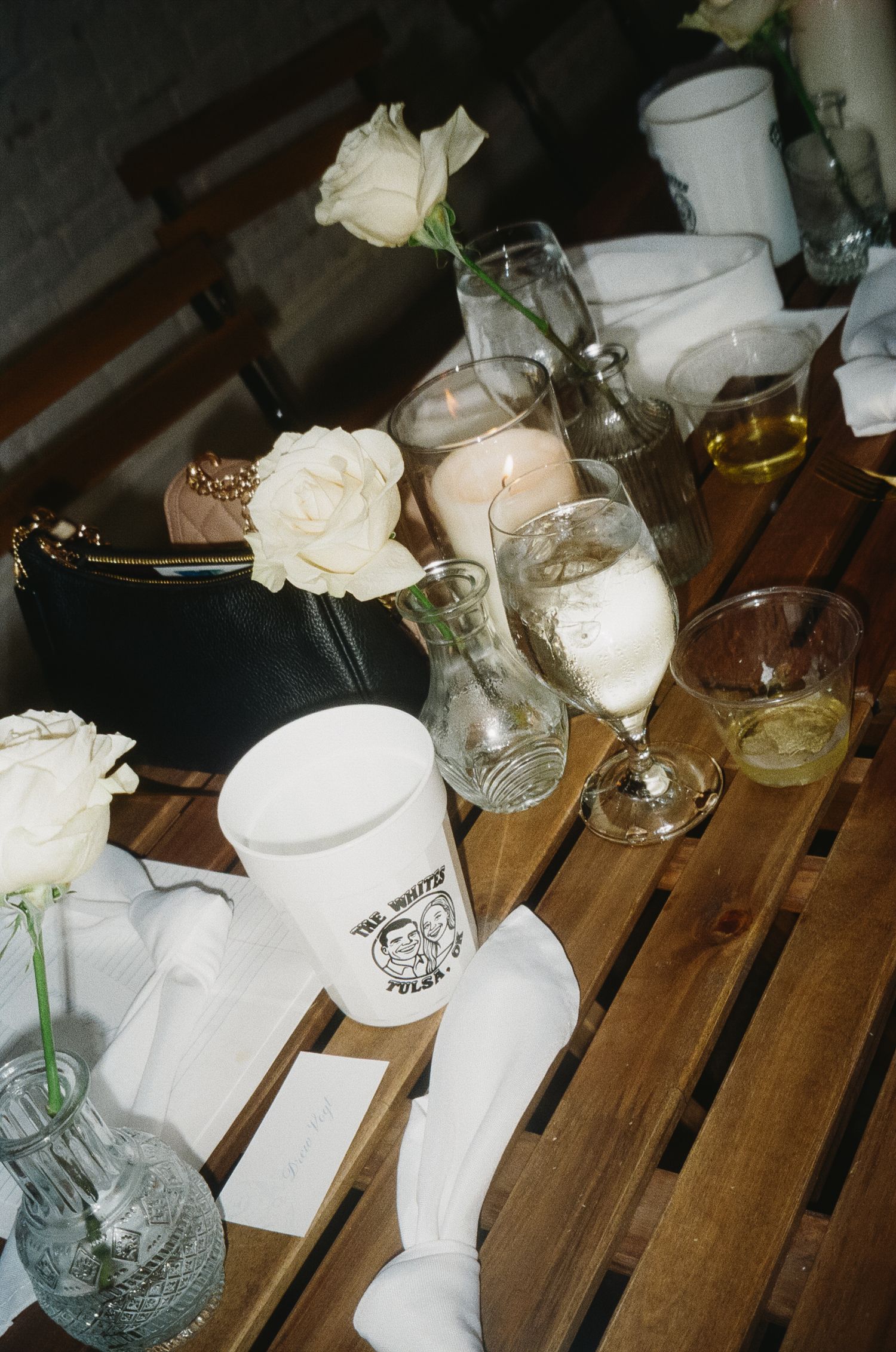 White table settings with roses and glassware arranged on wooden slats.