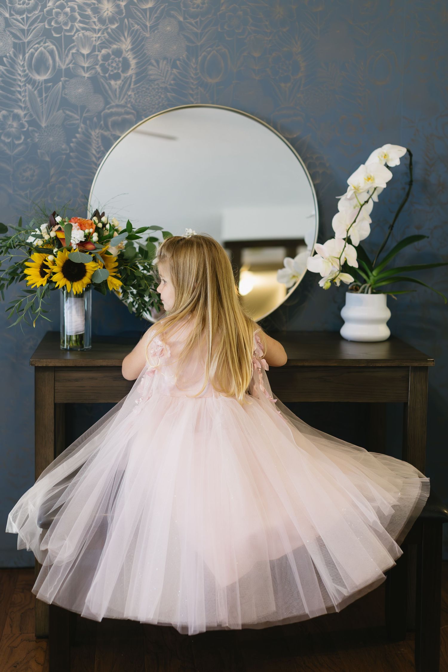 Pink tulle dress and white cowboy boots displayed against a dark wall with floral arrangements and decorative elements.