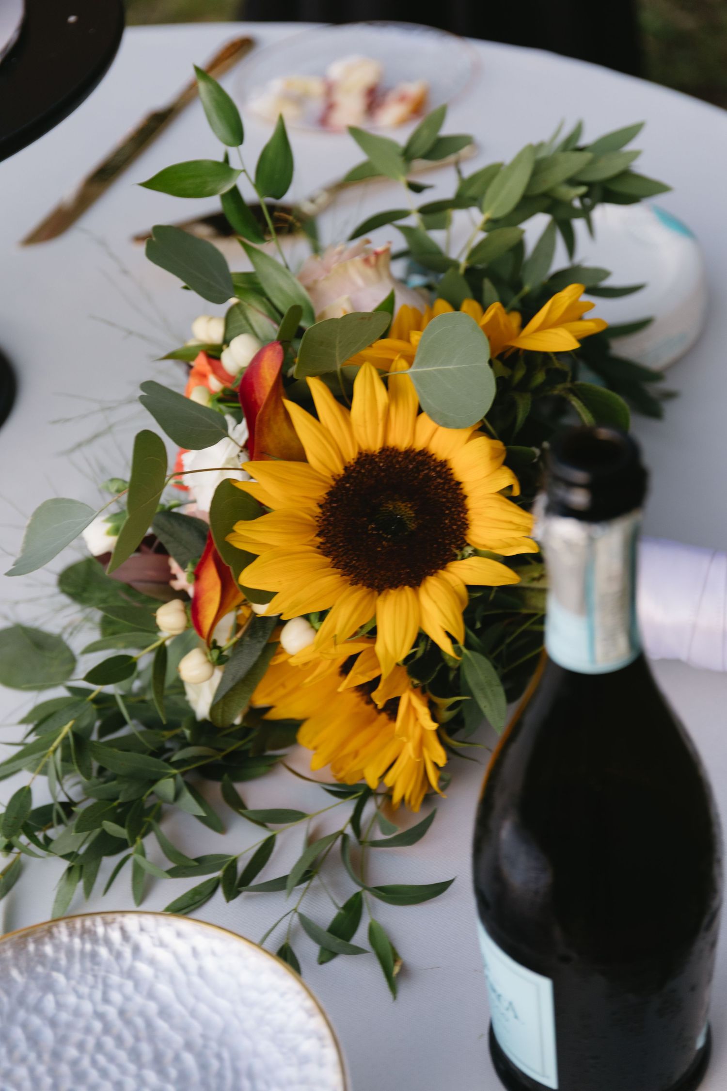 Sunflowers and greenery in black vases create elegant table centerpieces on white linens.