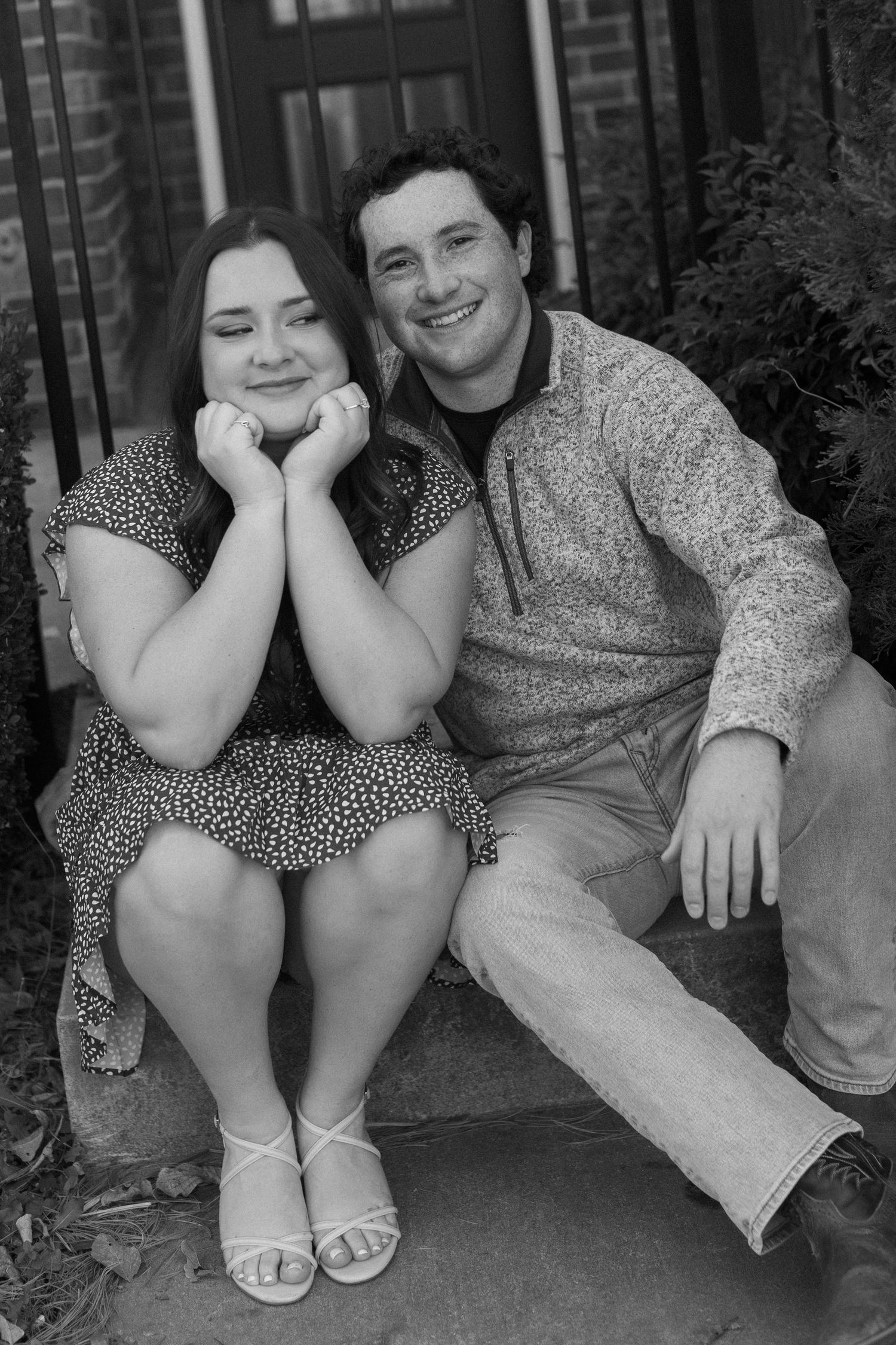 A couple sits together on outdoor steps sharing candid moments during a casual photoshoot.