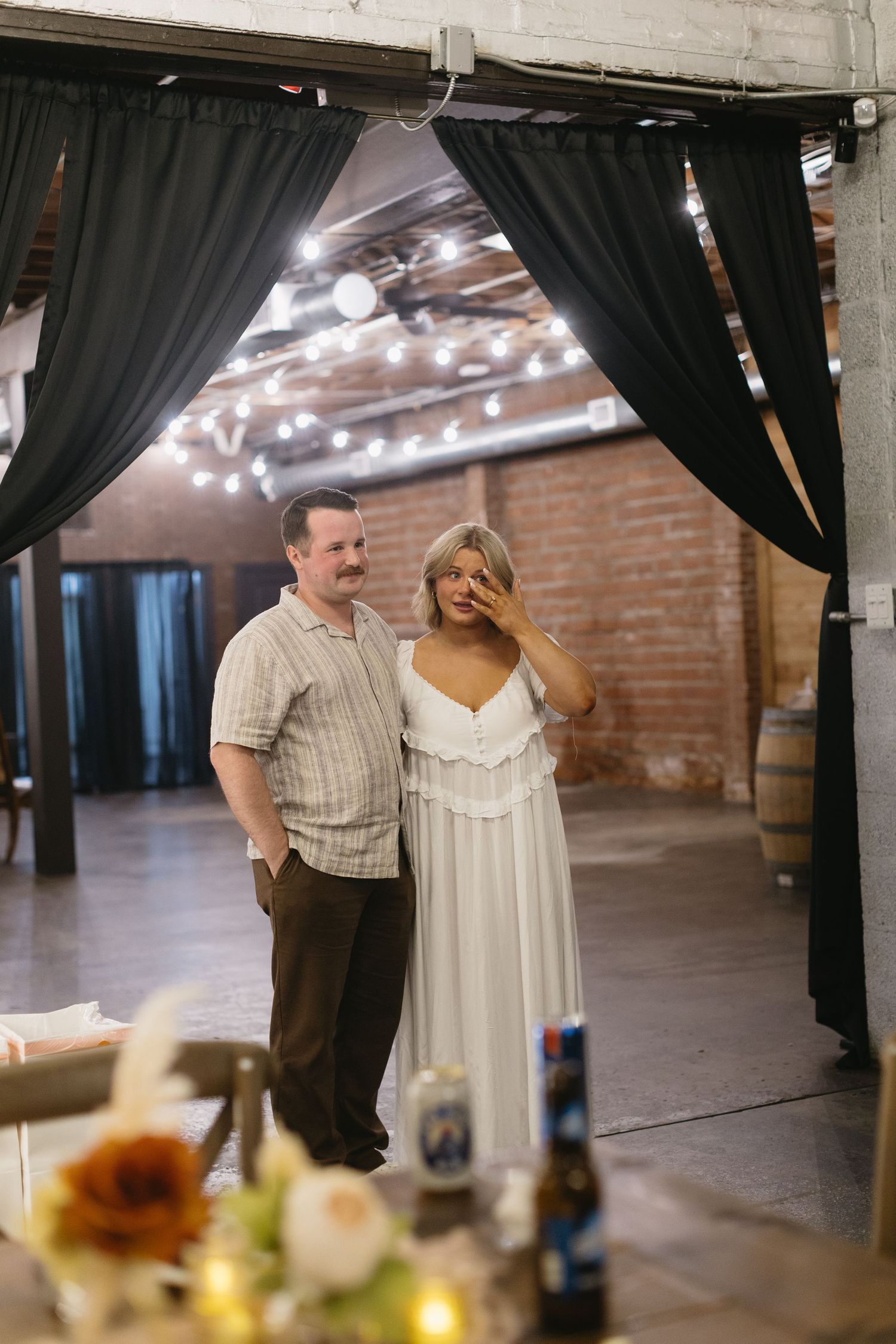 Couple sharing emotional moment under black curtains at rustic wedding venue.