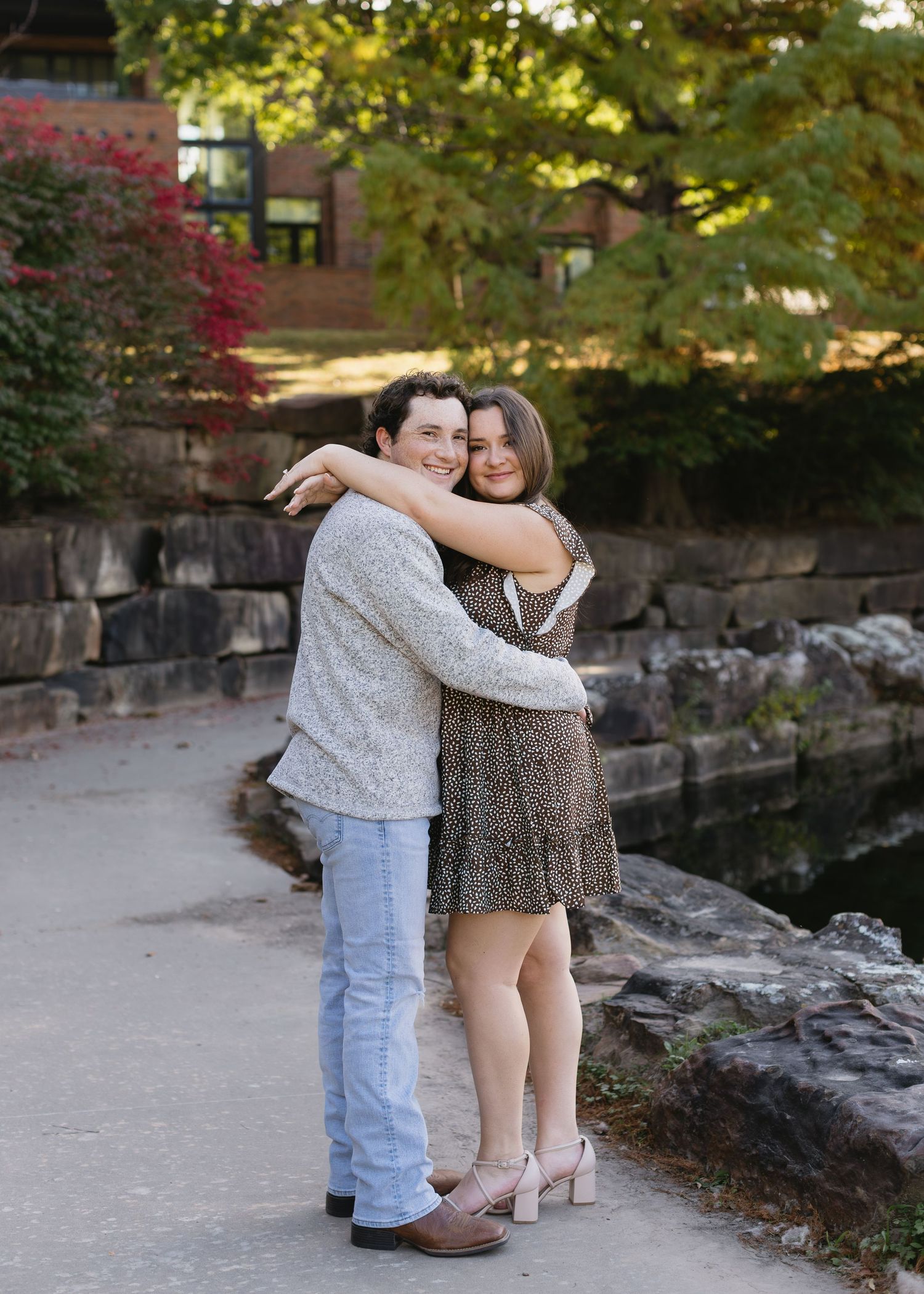 A couple embraces while standing on a stone path surrounded by fall foliage.
