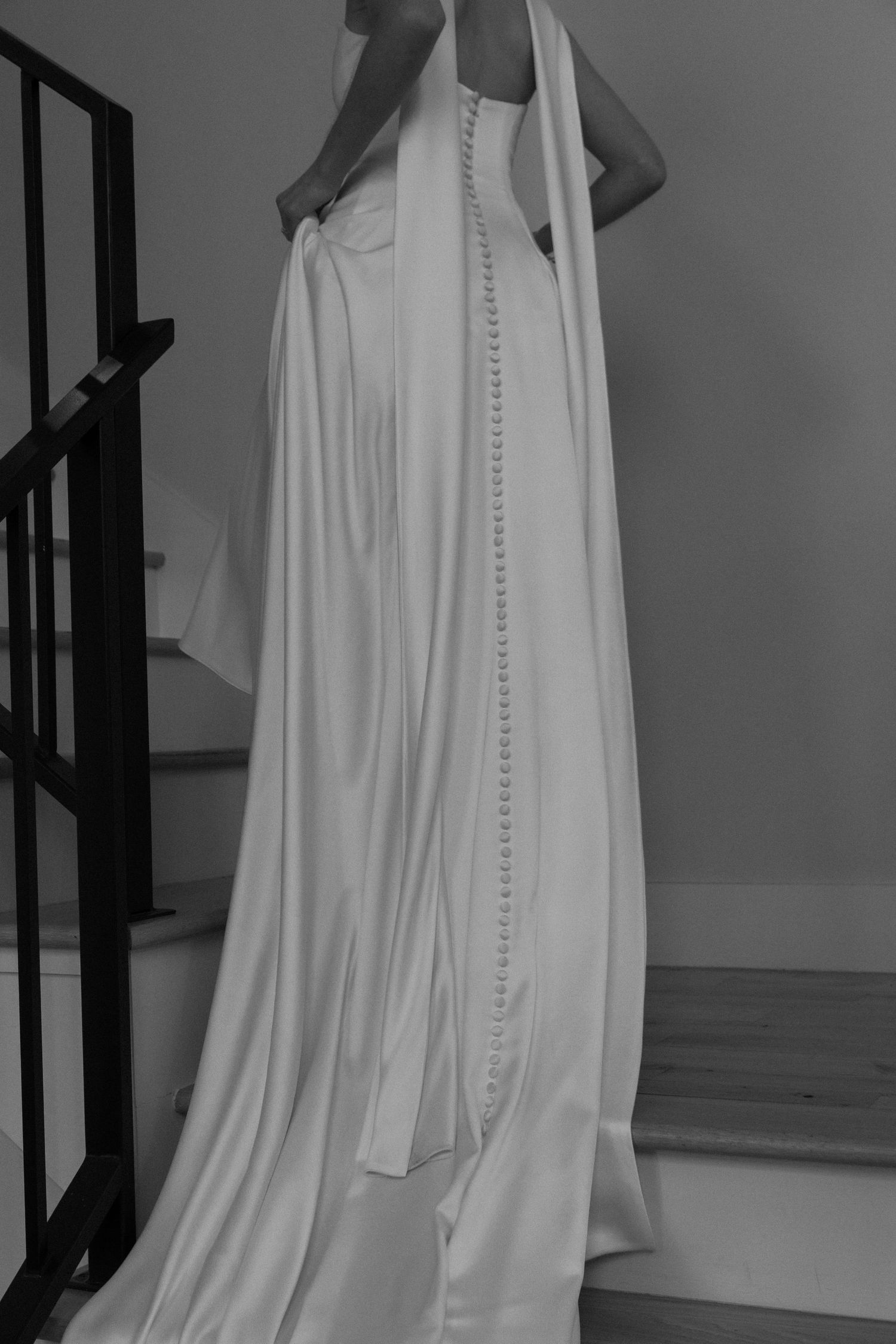 A flowing white wedding dress with elegant button details photographed from behind.