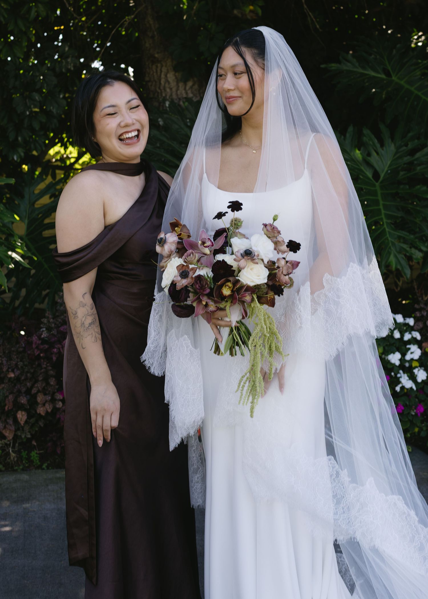 Wedding party in brown dresses gathered around bride in white gown with floral bouquet.