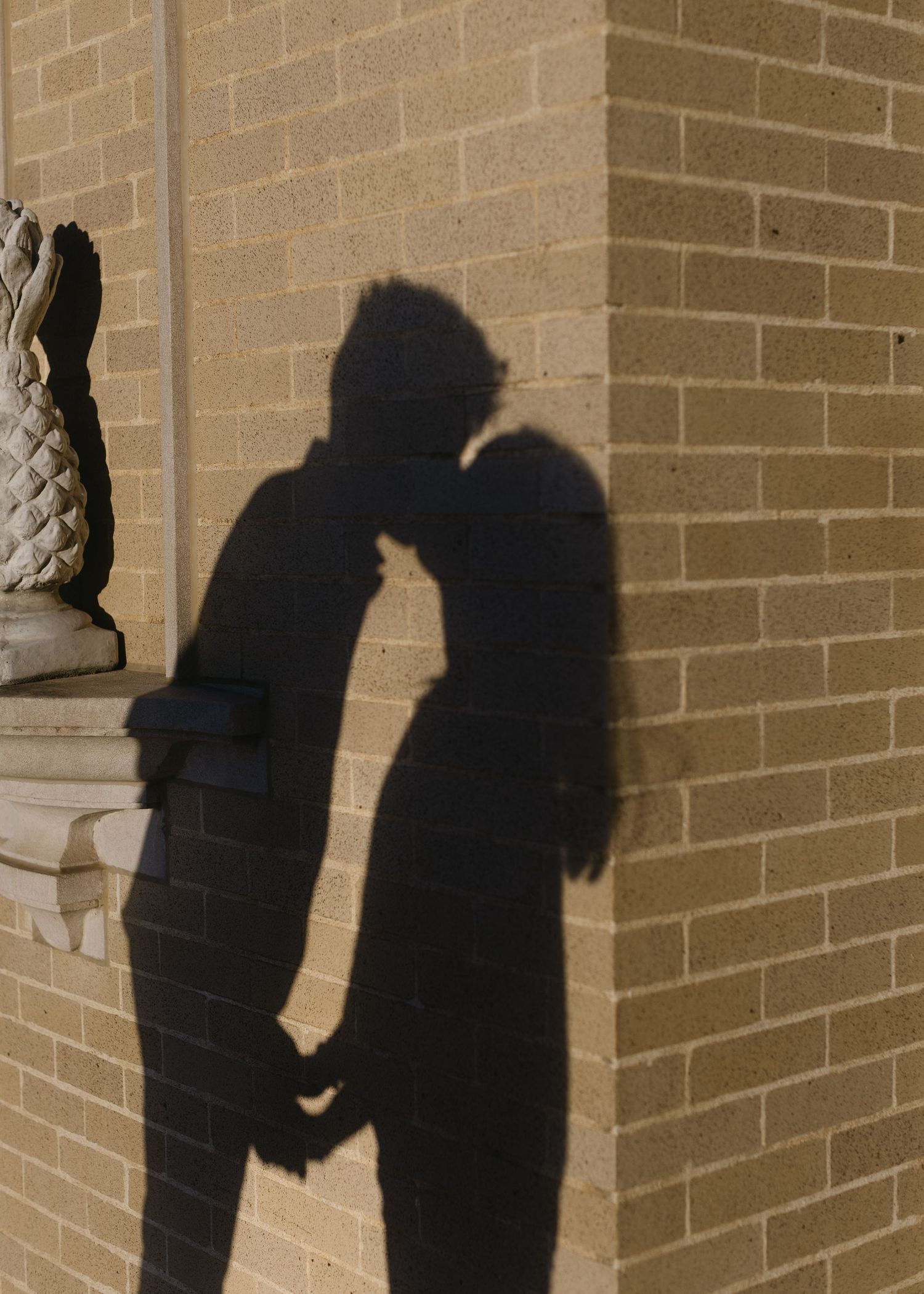 Silhouettes of two figures cast shadows against a brick wall in a sequence of progressive movements.