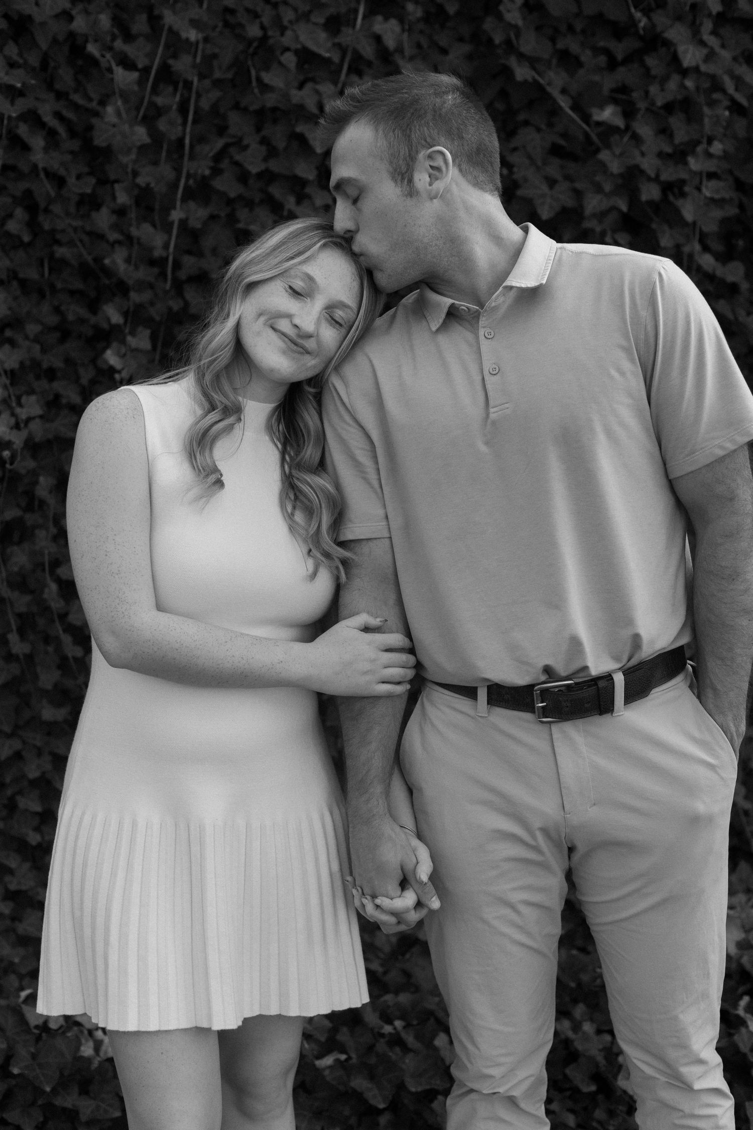 A romantic couple in light and dark clothing embrace outdoors against a dark foliage background in a photo series.