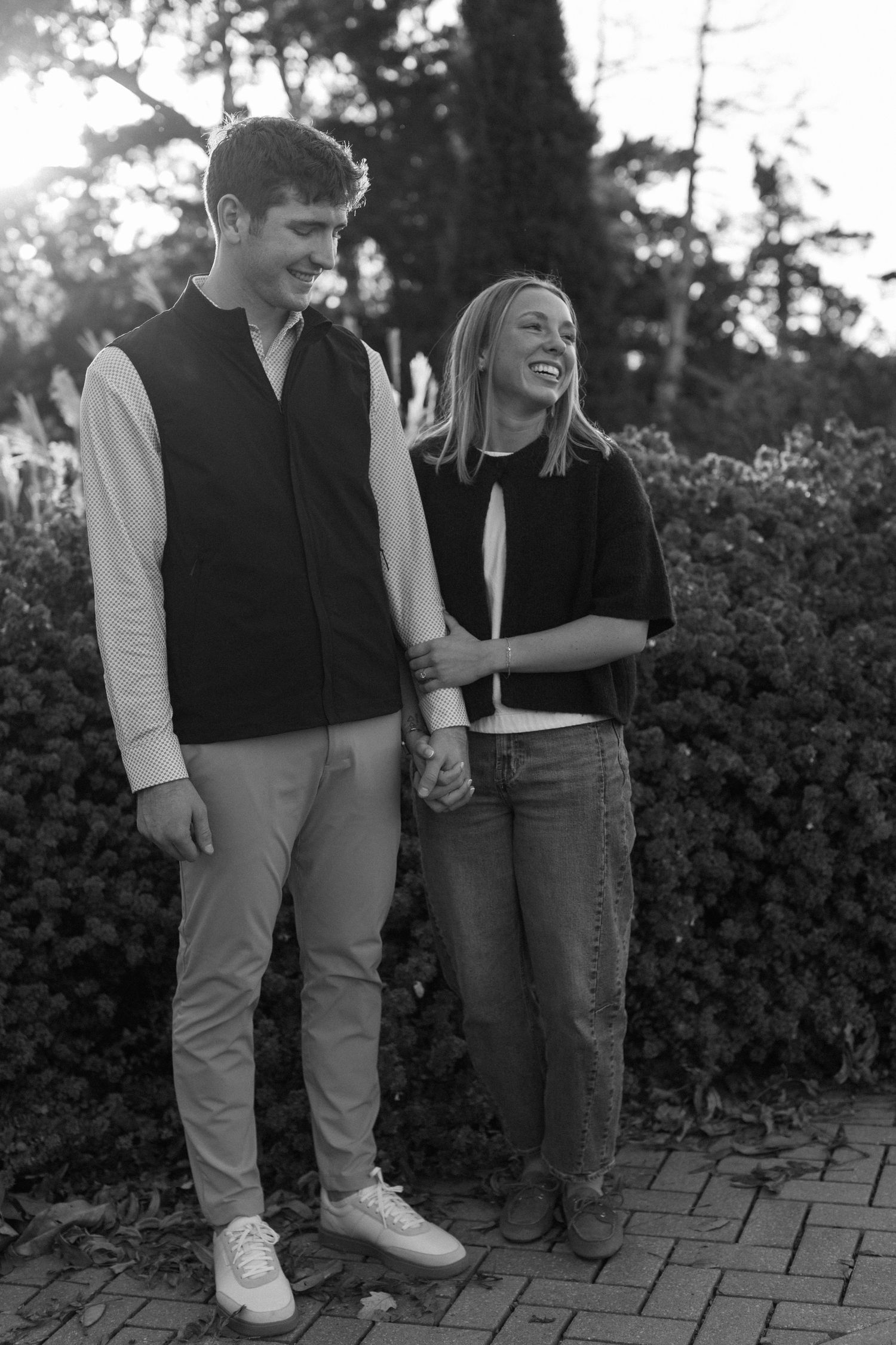 A couple shares a candid laughing moment together on a brick pathway.