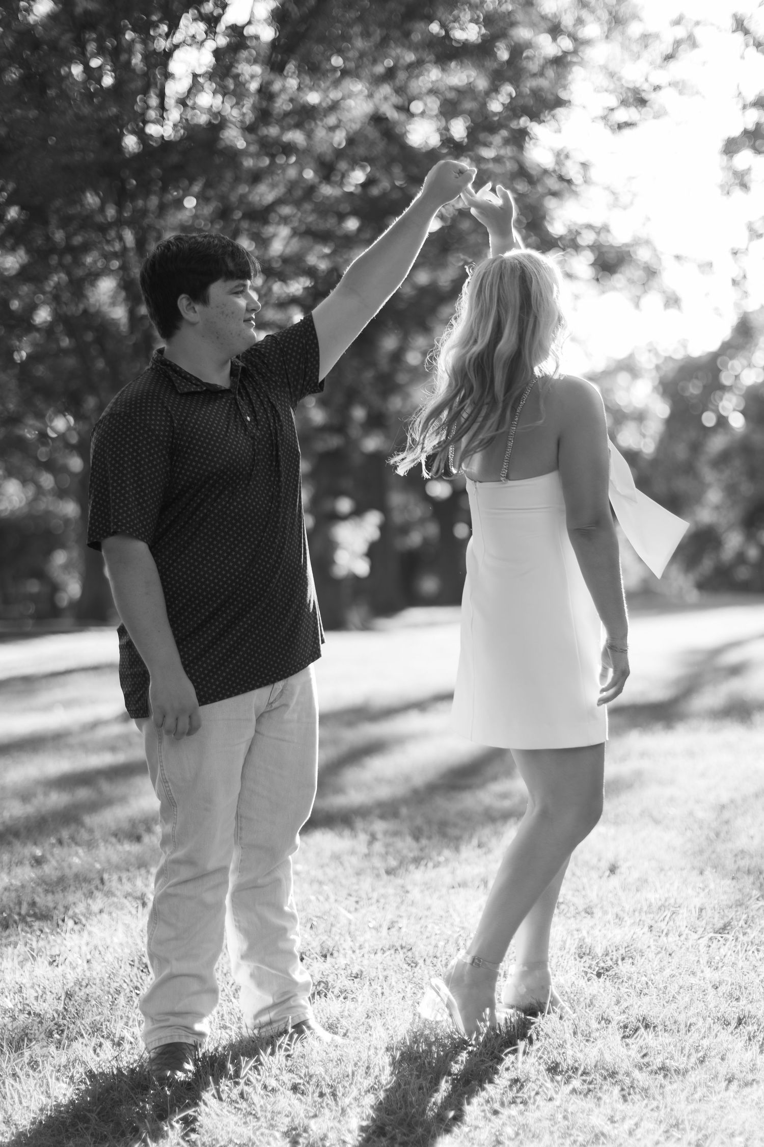 A couple walks together in a grassy sunlit field sharing intimate moments in black and white.