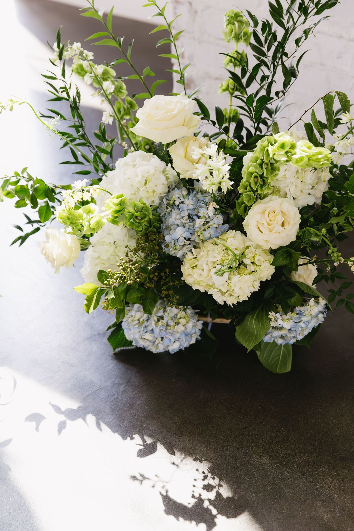 Elegant white and blue flower arrangements with hydrangeas and roses displayed on a dark surface.