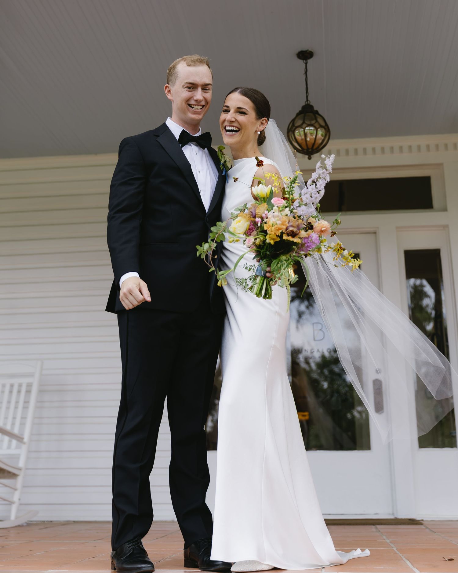 Wedding couple sharing joyful moments on a white porch during their special day celebration.