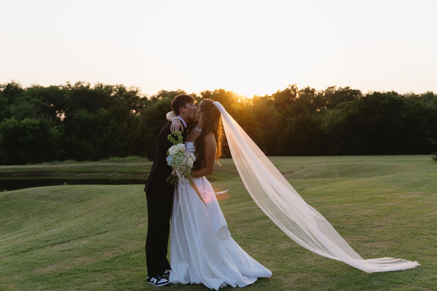 A couple embraces during their sunset wedding ceremony on a lush golf course with a long flowing veil.