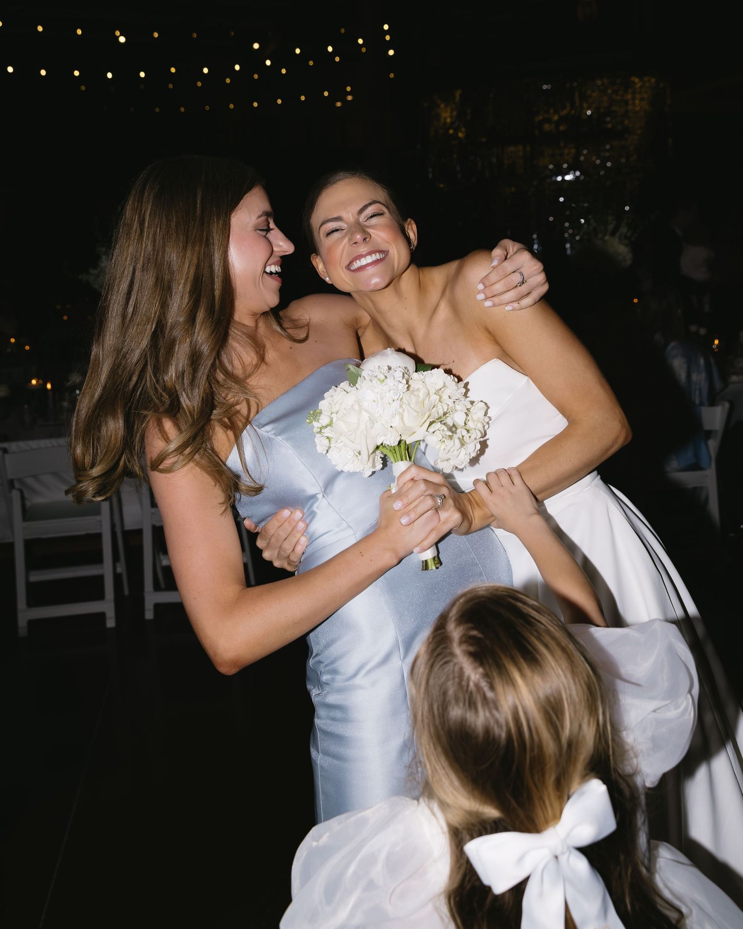 Wedding celebration moment captured with white bouquets and string lights in evening setting.