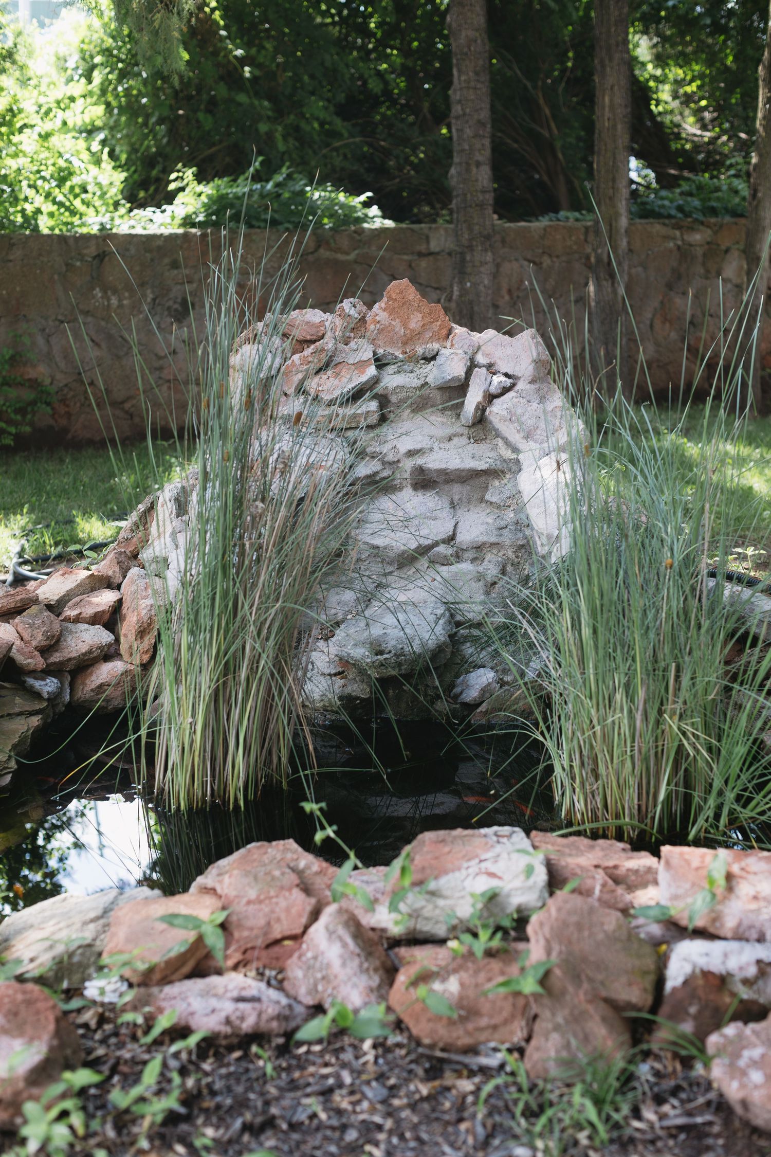 Natural stone waterfall feature with tall grasses in a garden setting.