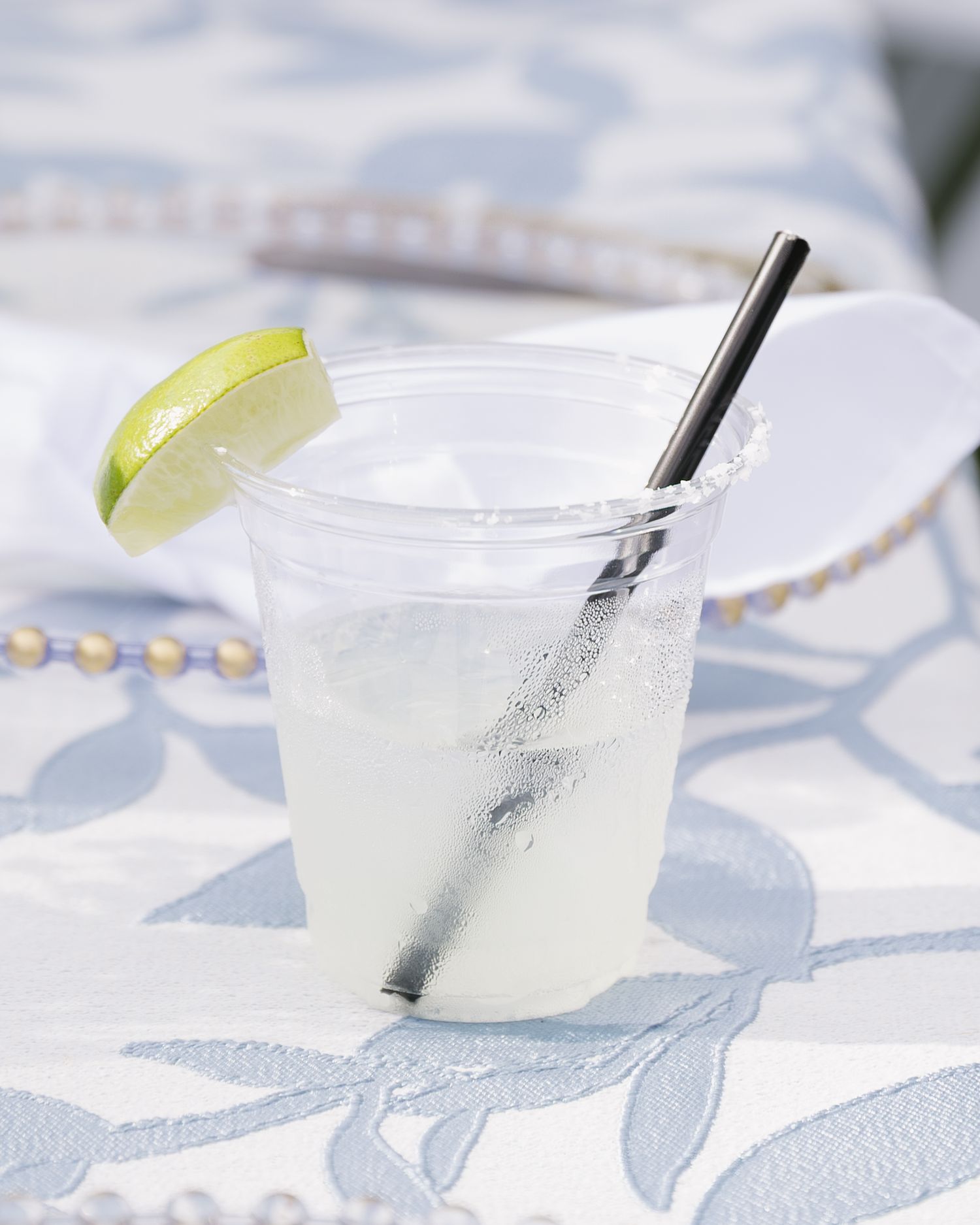 Row of refreshing margarita cocktails garnished with lime slices on a patterned tablecloth.