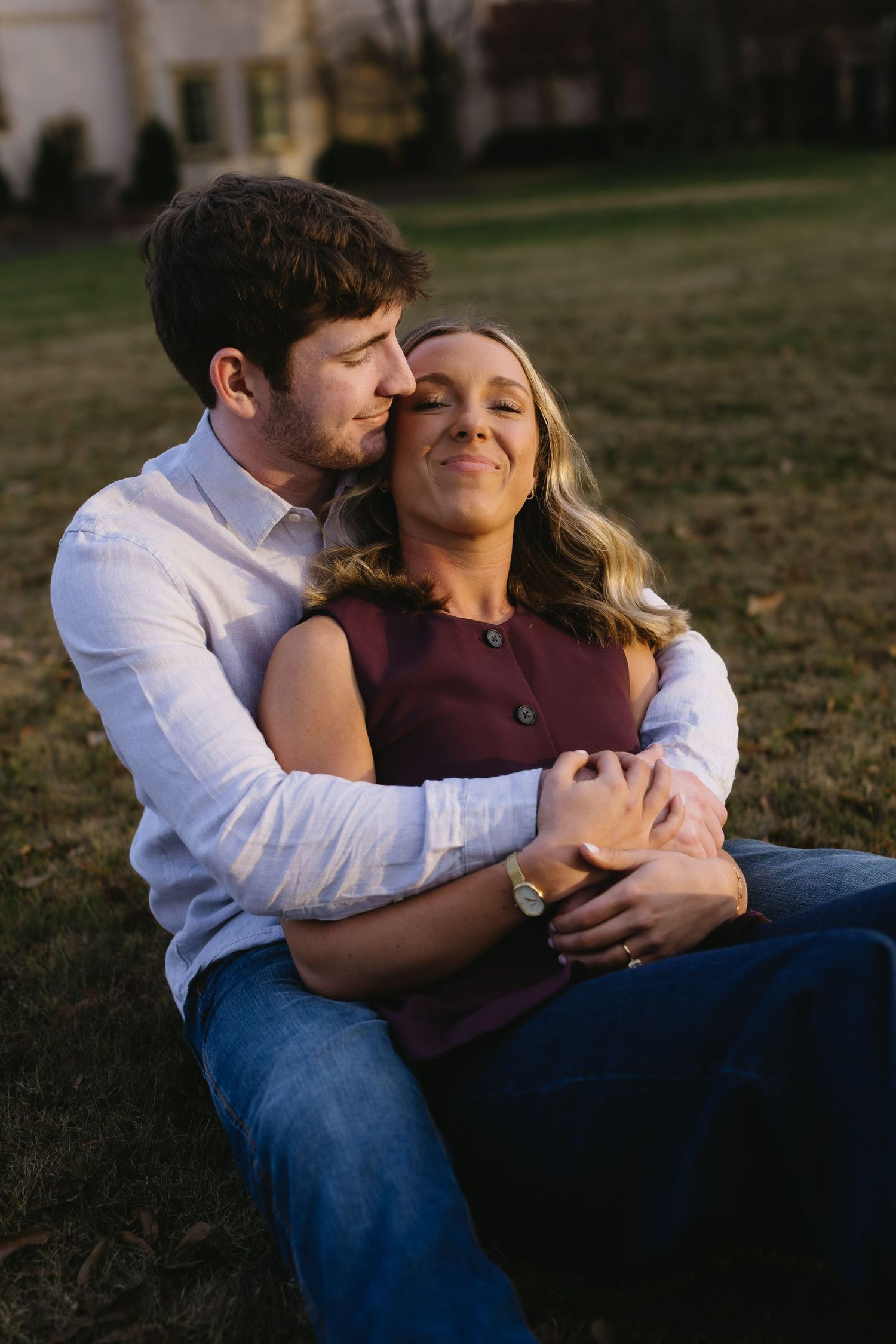 A tender embrace between a couple sitting on grass during golden hour.