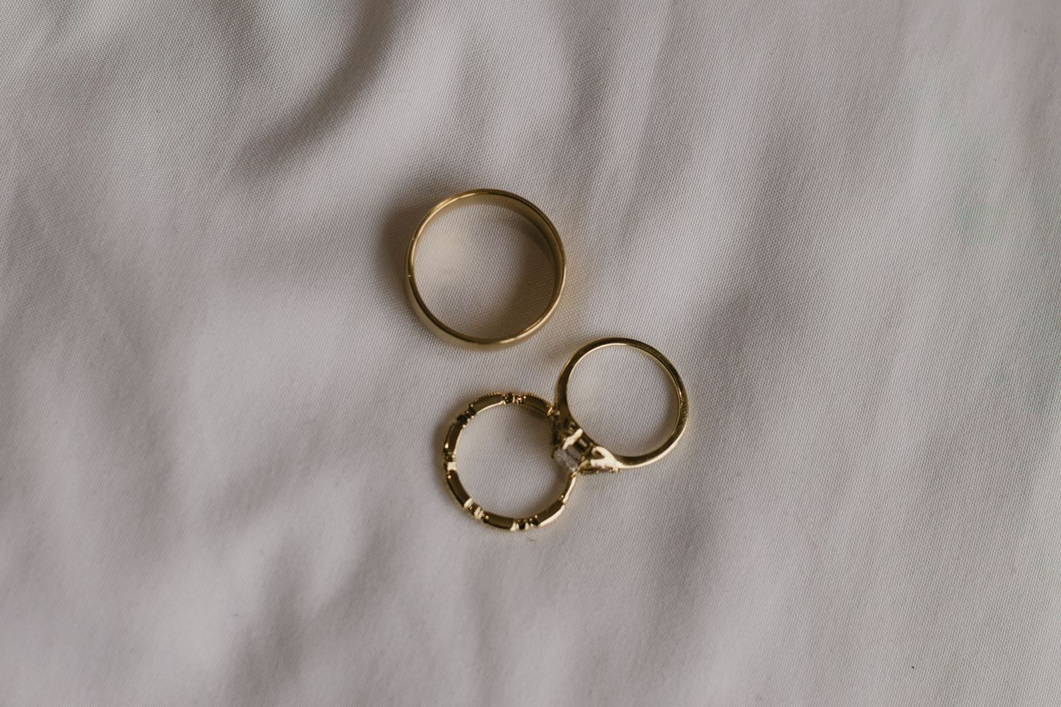 Two gold wedding rings rest on a soft white surface in natural lighting.