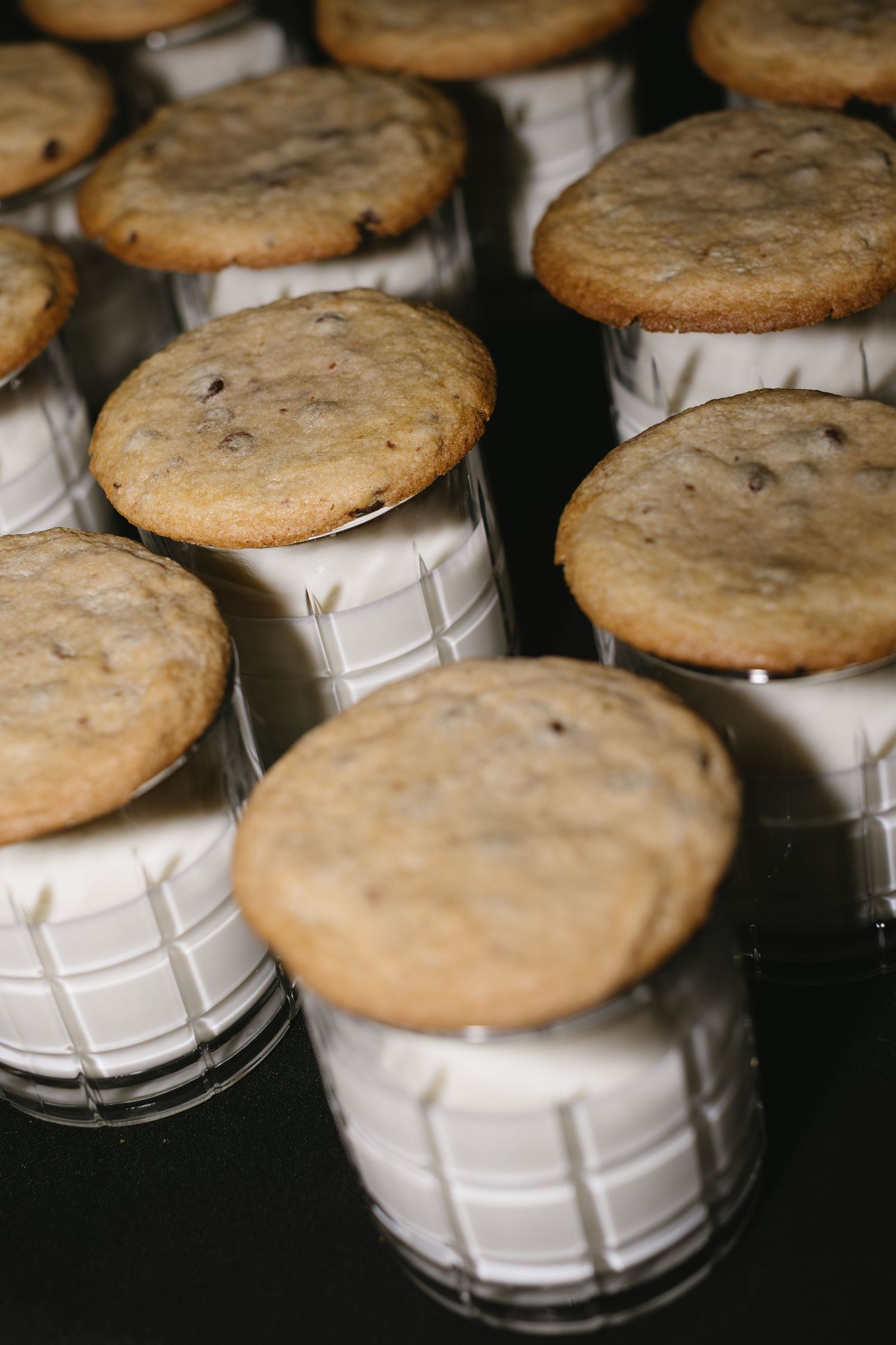 Chocolate chip cookies arranged on white ceramic jar lids in a dark setting.