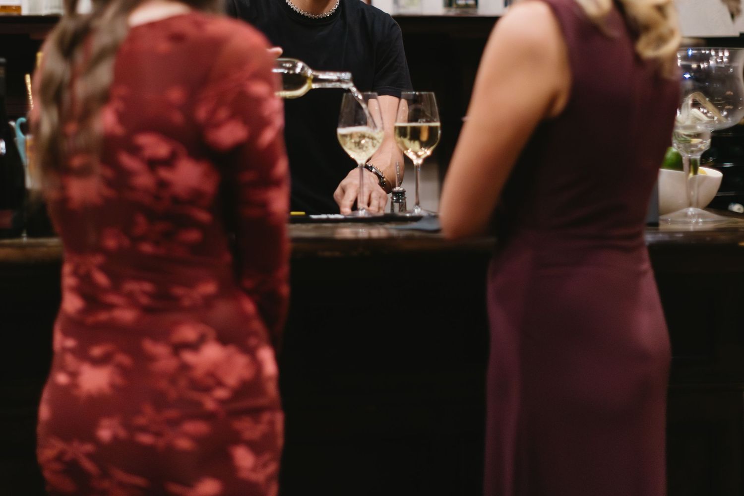 A group of people in burgundy dresses stand together at a formal event with wine glasses in hand.