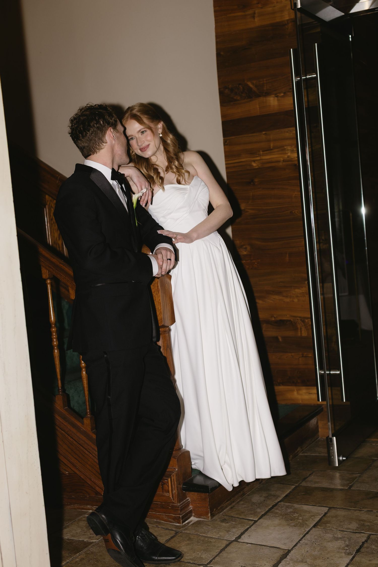 Couple dancing intimately in formal attire against wooden paneled walls.