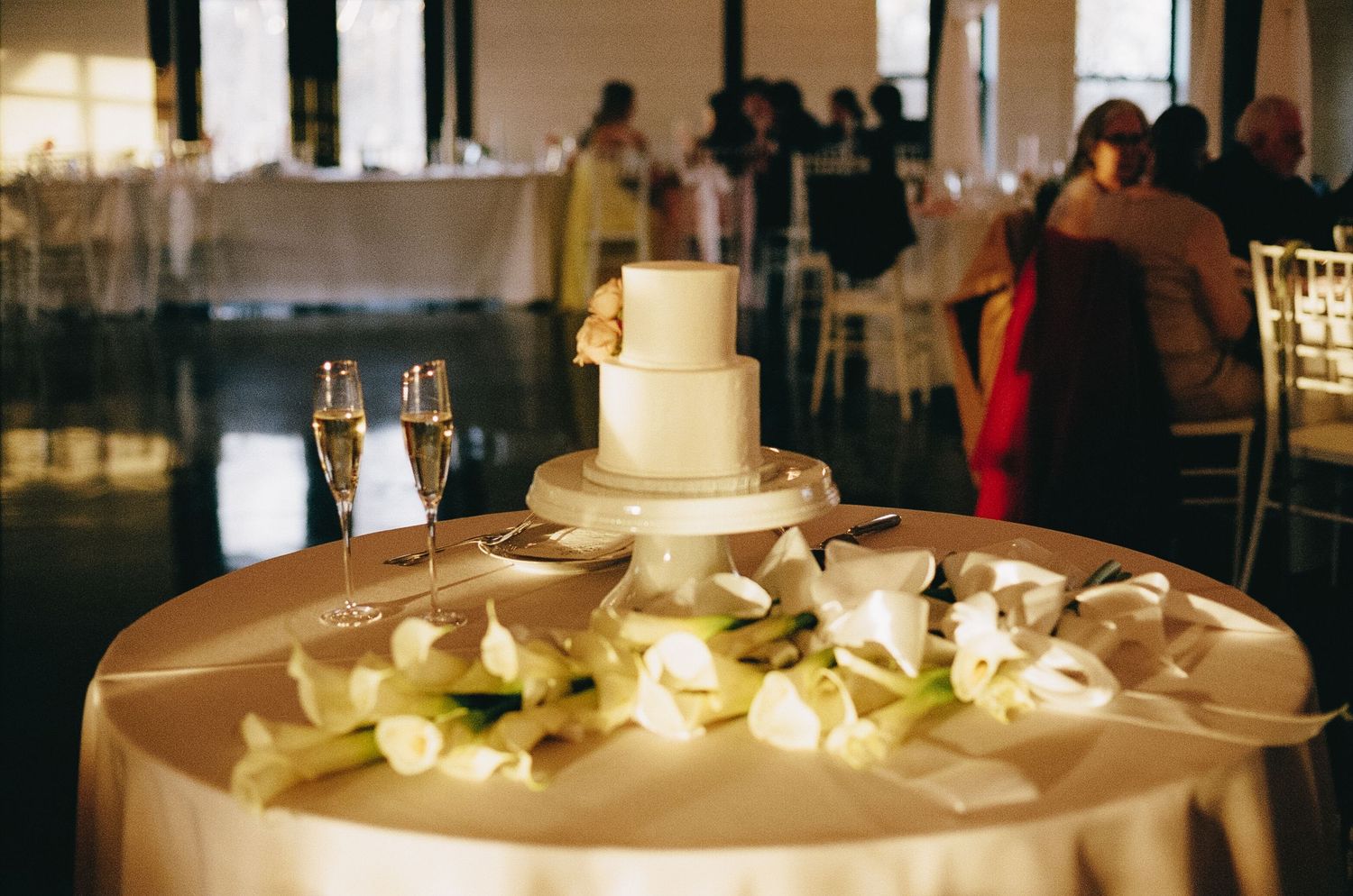 A white wedding cake adorned with delicate orchids and illuminated by soft candlelight at an elegant reception.