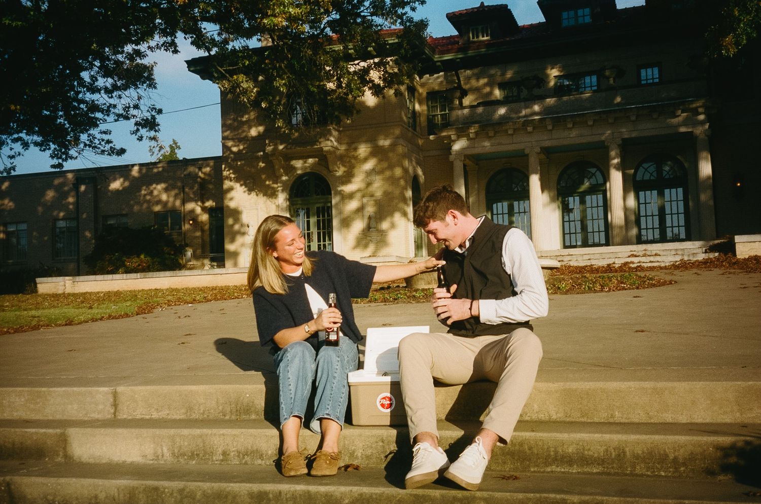 A couple shares a romantic moment while sitting on outdoor steps at a stately building.
