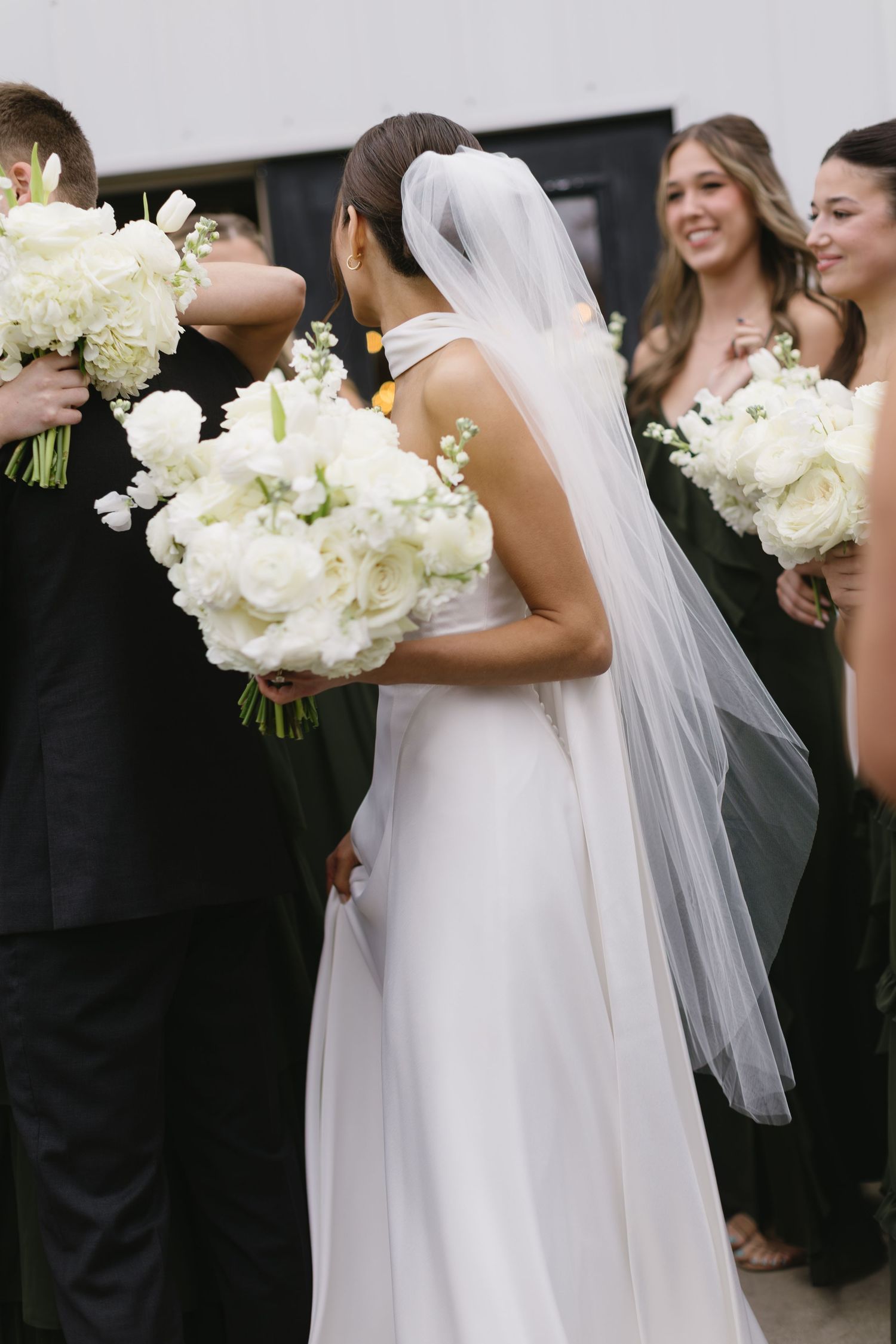 Wedding party members hold elegant white hydrangea bouquets while standing together outdoors.