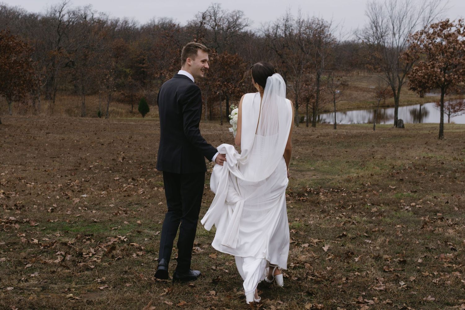 Wedding couple and guests walk through a scenic autumn field during celebration.