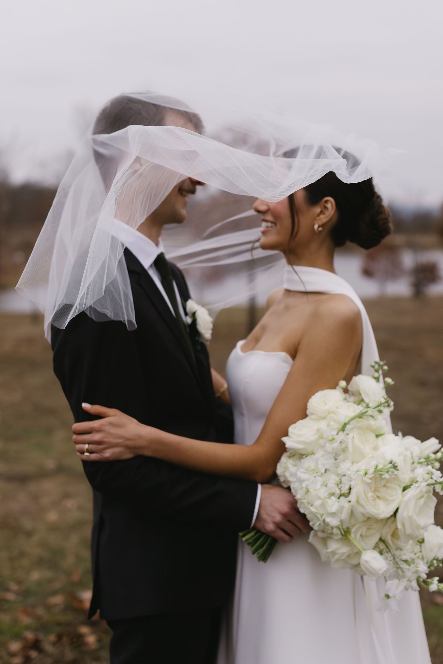 Romantic wedding moment captured as couple embraces with flowing veil and white bouquet.