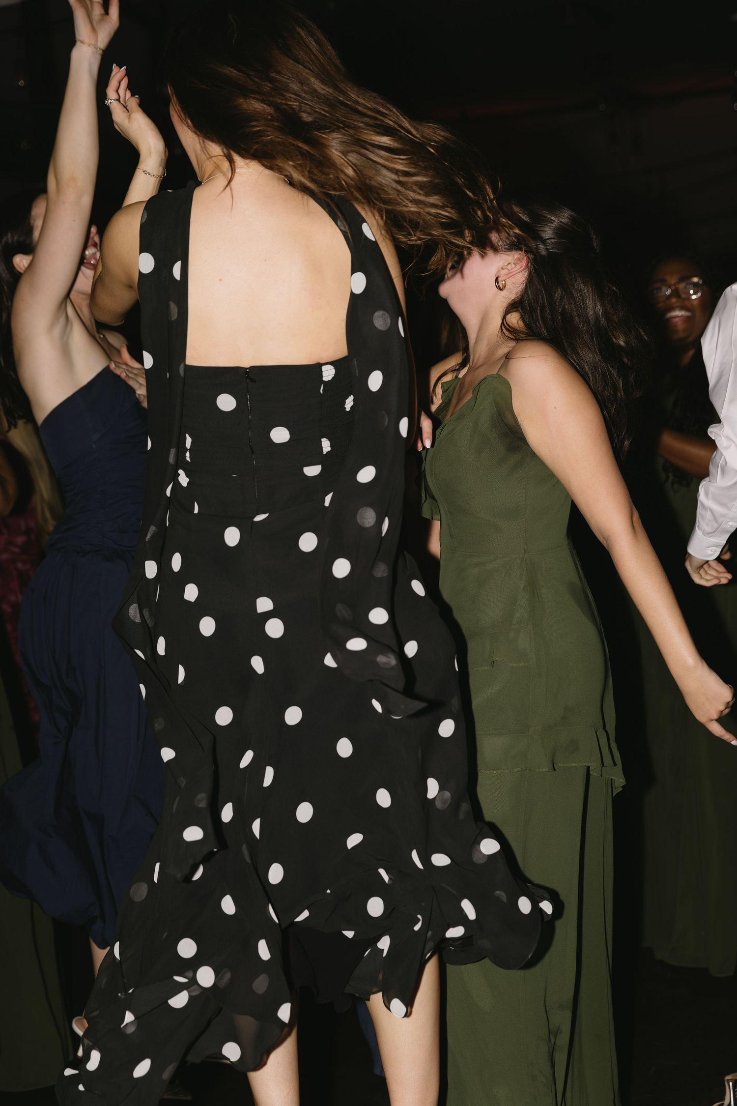 People dancing and celebrating at a party wearing polka dot and olive green dresses.