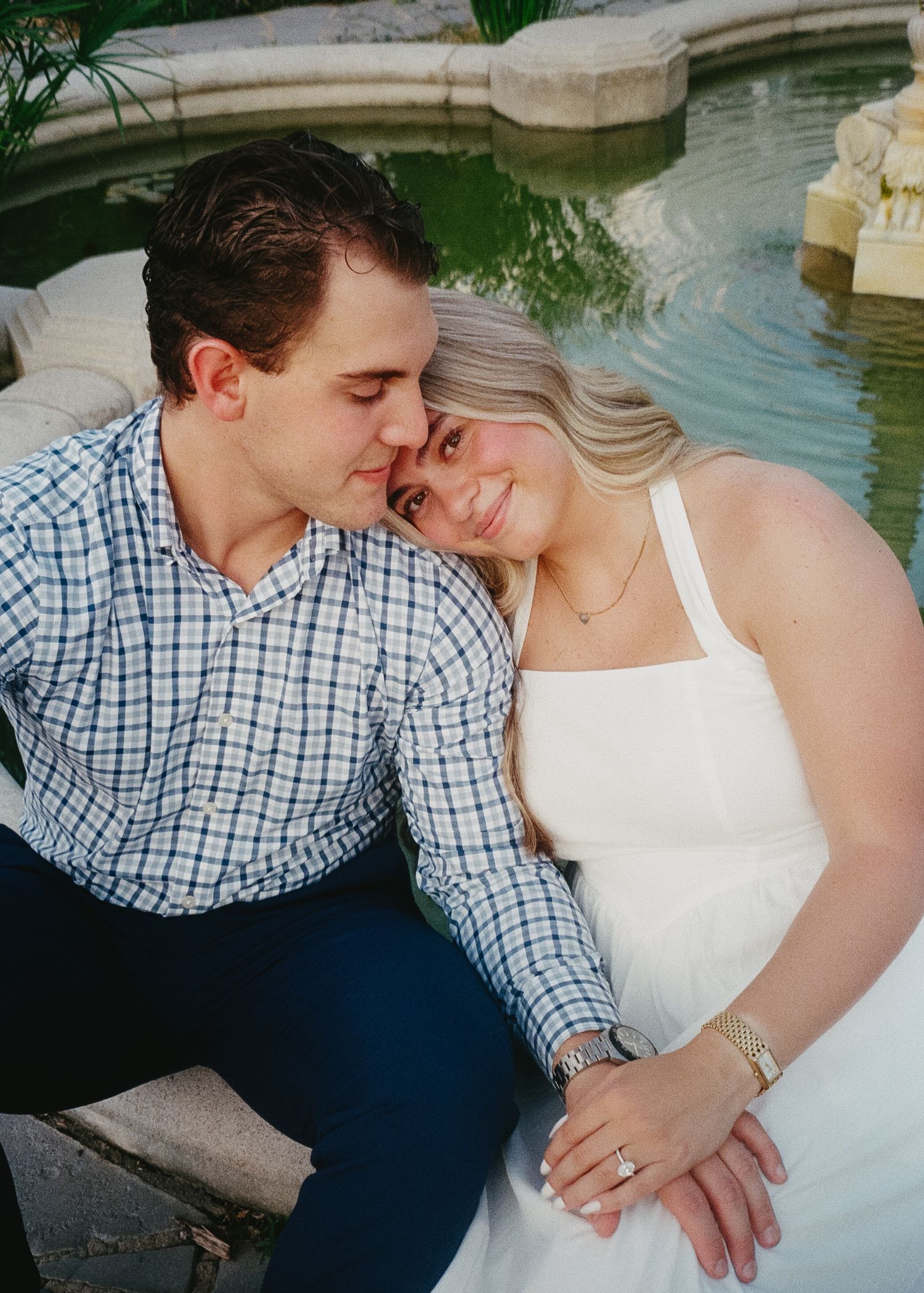A romantic couple in formal attire shares intimate moments by a reflective pool during a photo session.