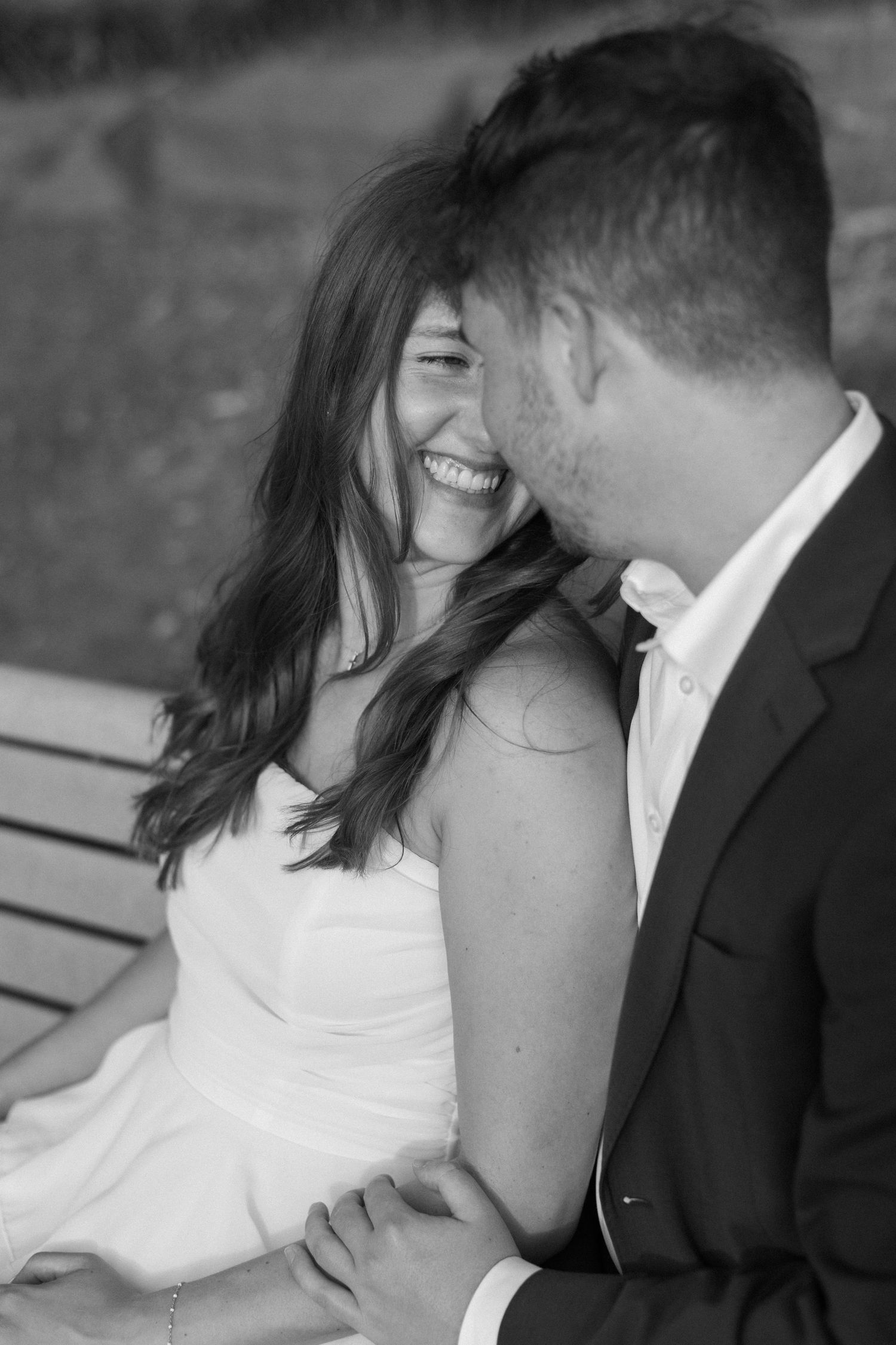 A romantic black and white candid moment of a couple sharing laughter while sitting close together.