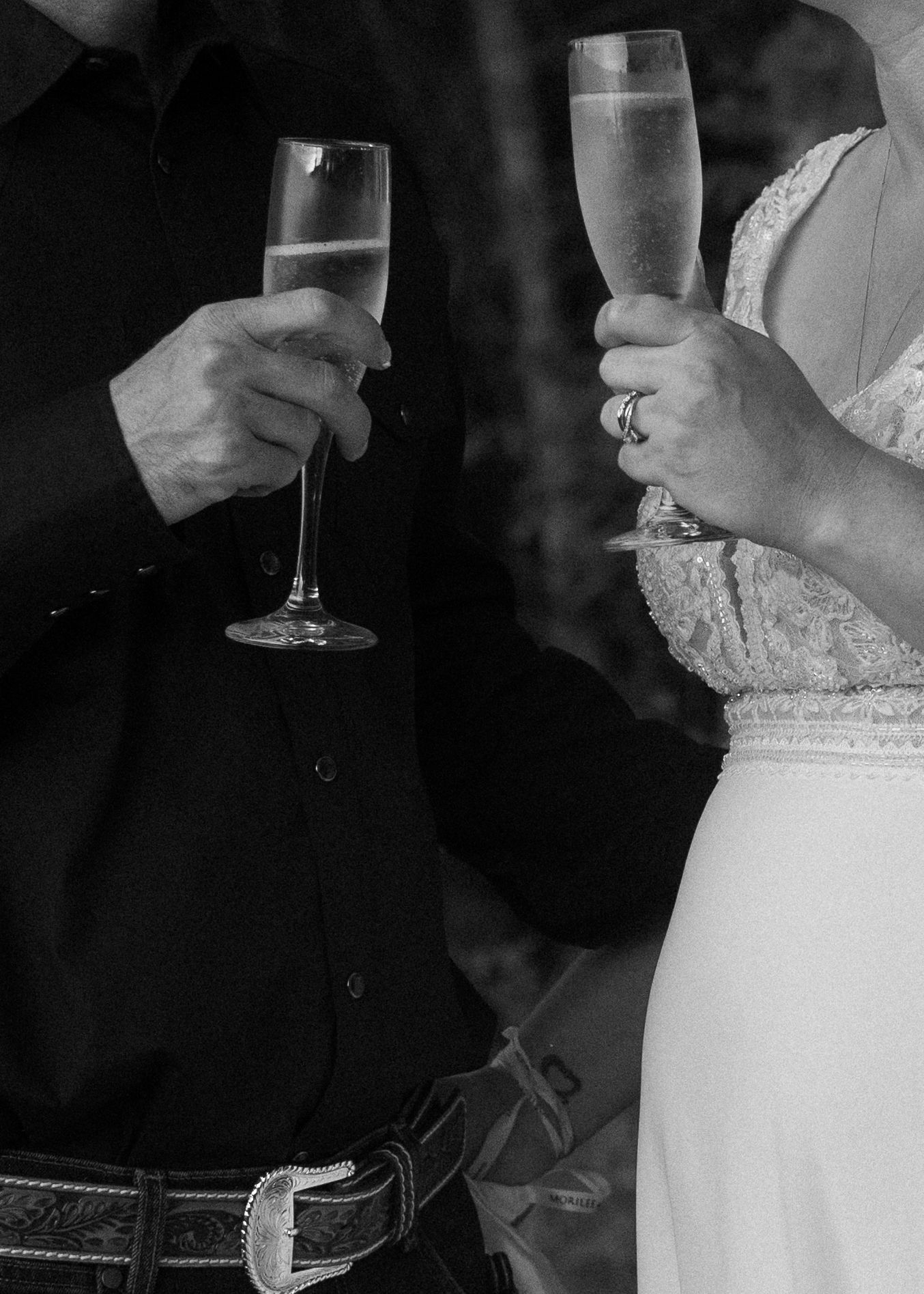 Close-up of champagne glasses being held during a wedding toast in black and white.