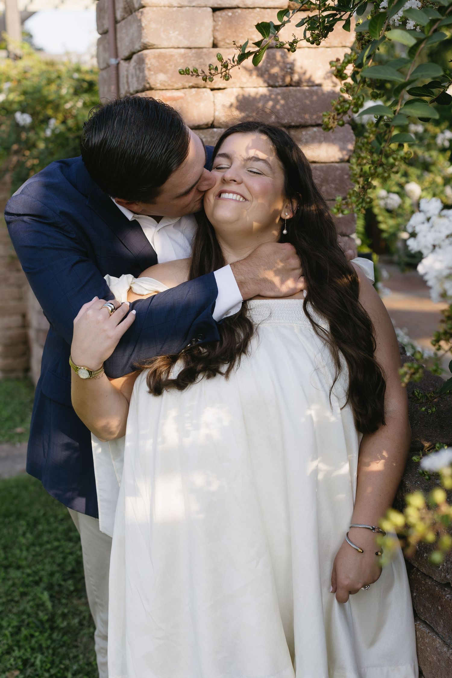 A romantic candid moment between a couple in white and navy attire against a stone backdrop.