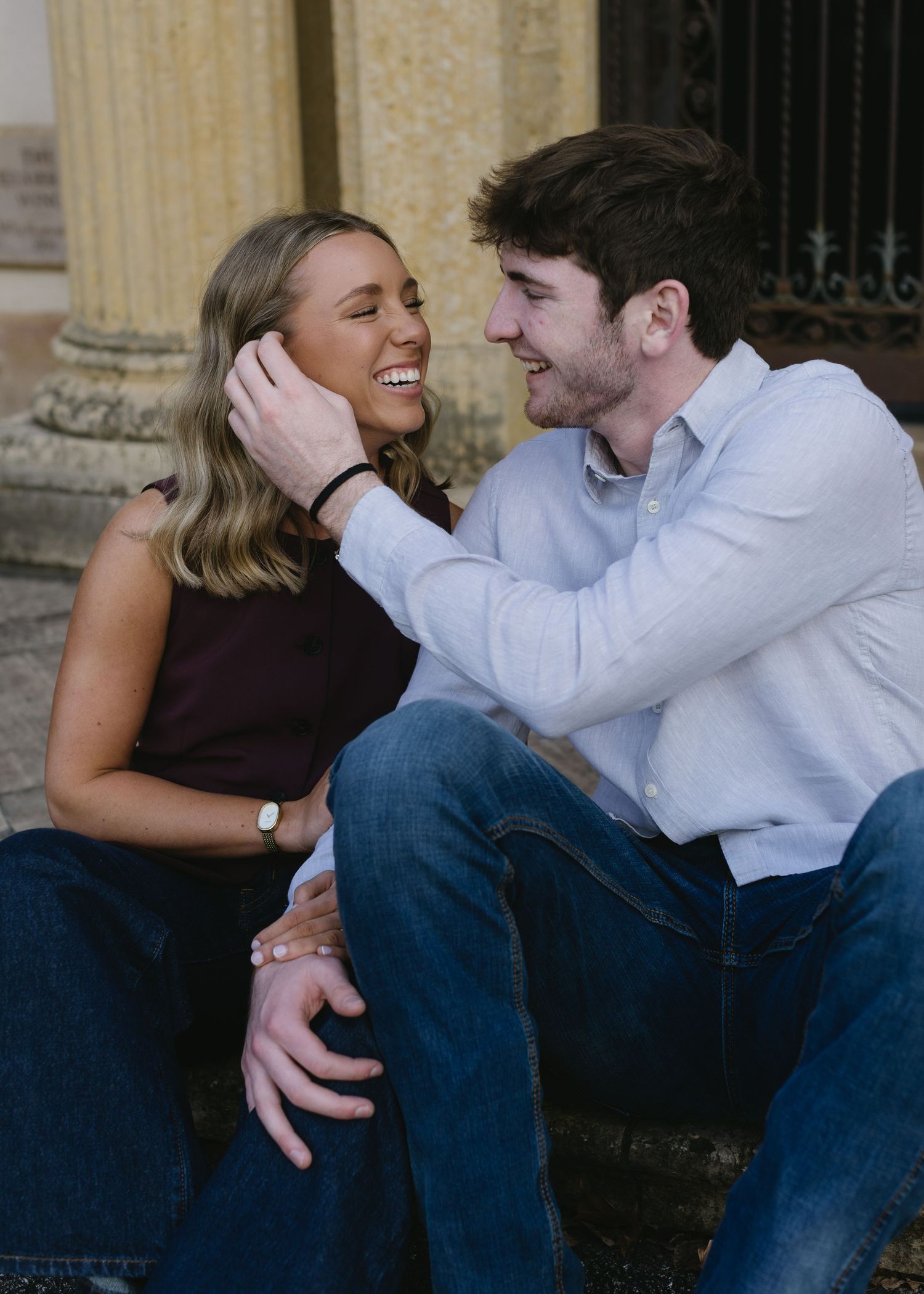 A couple shares an intimate moment while sitting together outdoors near classical architecture.