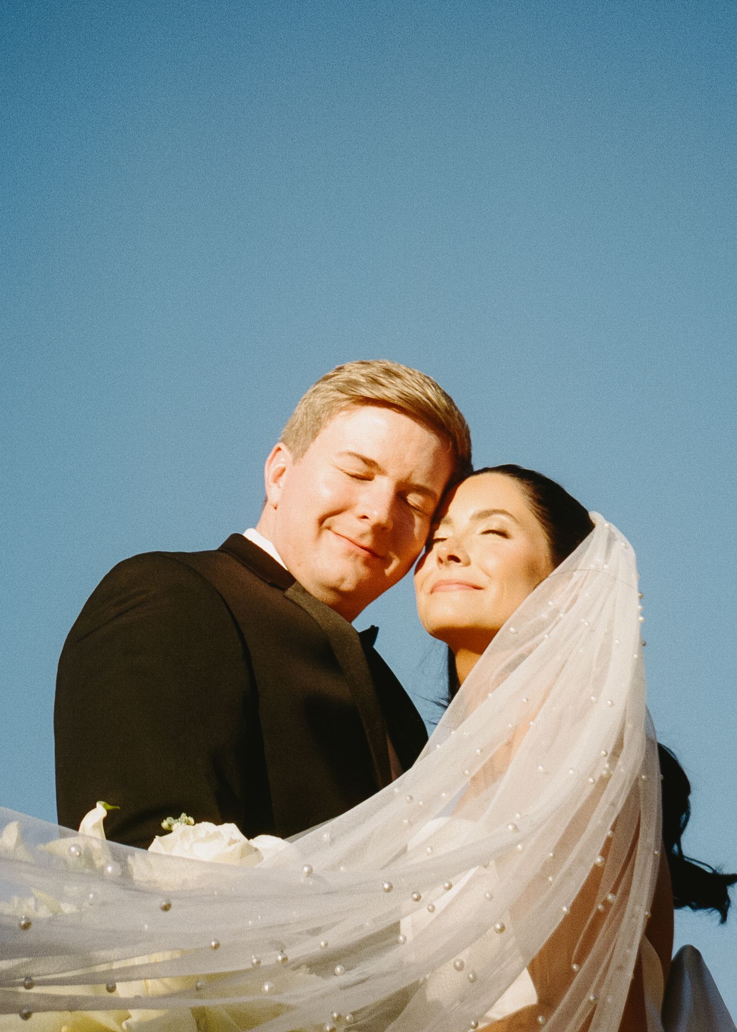 Romantic outdoor portrait against blue sky with flowing bridal veil.