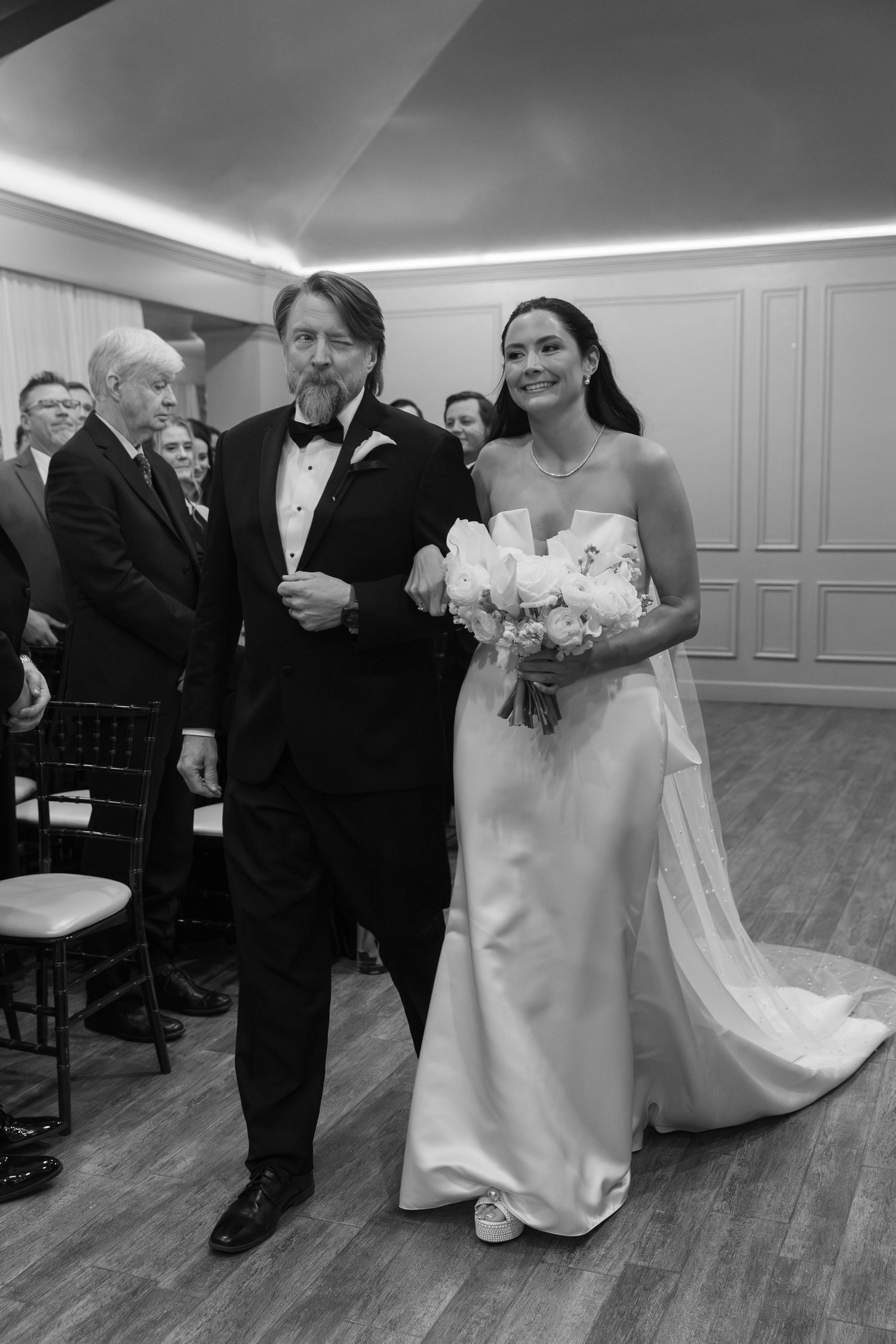 Wedding party in formal attire gathers in an elegant room with hardwood floors.