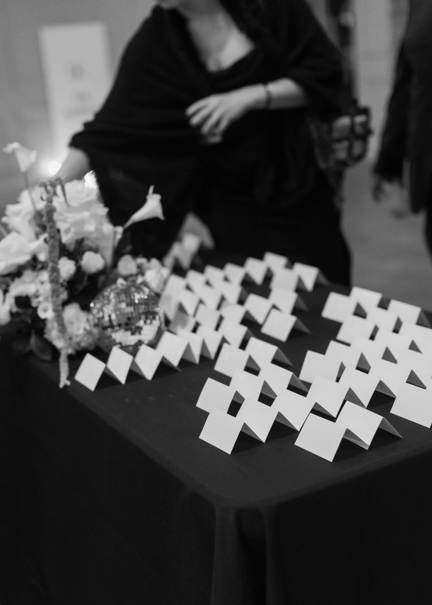 Black and white photo of place cards arranged on table next to floral arrangement.