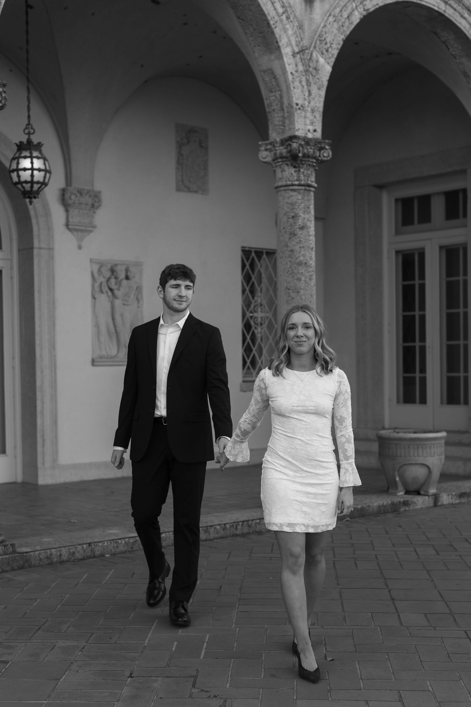 A couple walking together through an elegant stone colonnade.