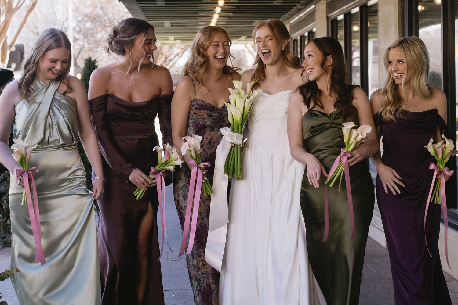 Wedding party in coordinated dresses of green and purple holding floral bouquets while walking together.