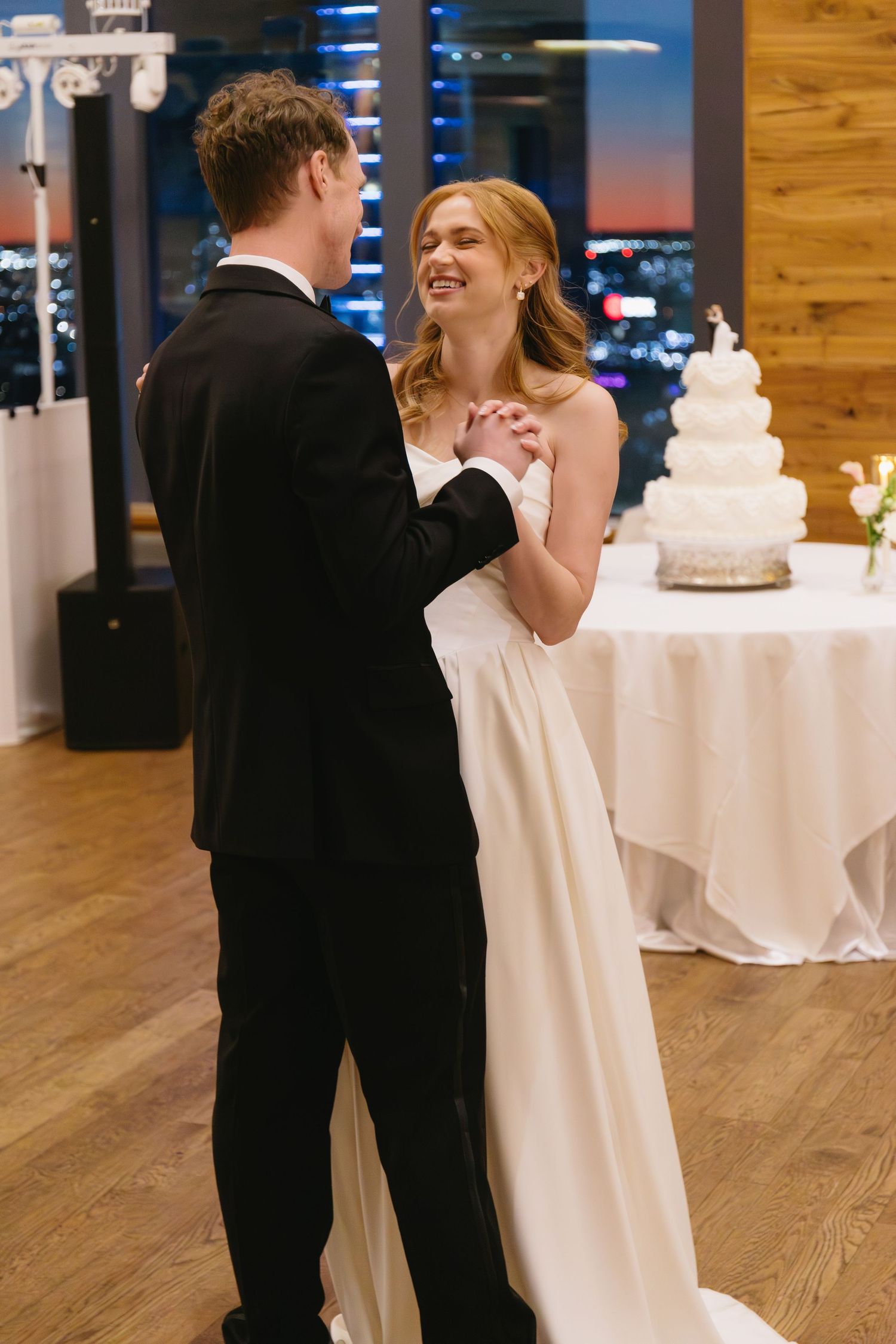 Wedding couple dancing near white-clothed tables and tiered wedding cake.