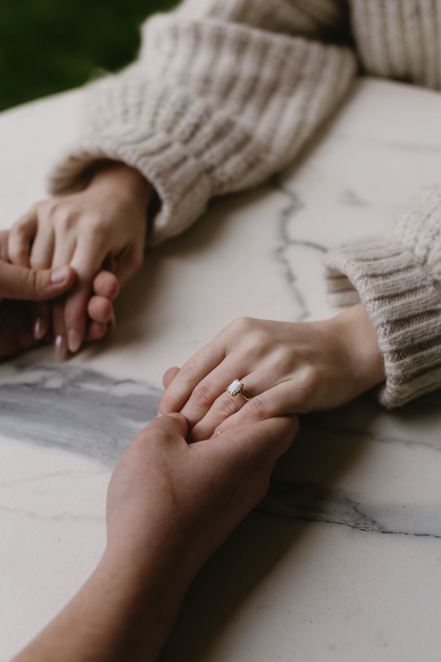 Close-up view of hands holding each other tenderly against a white marble surface.