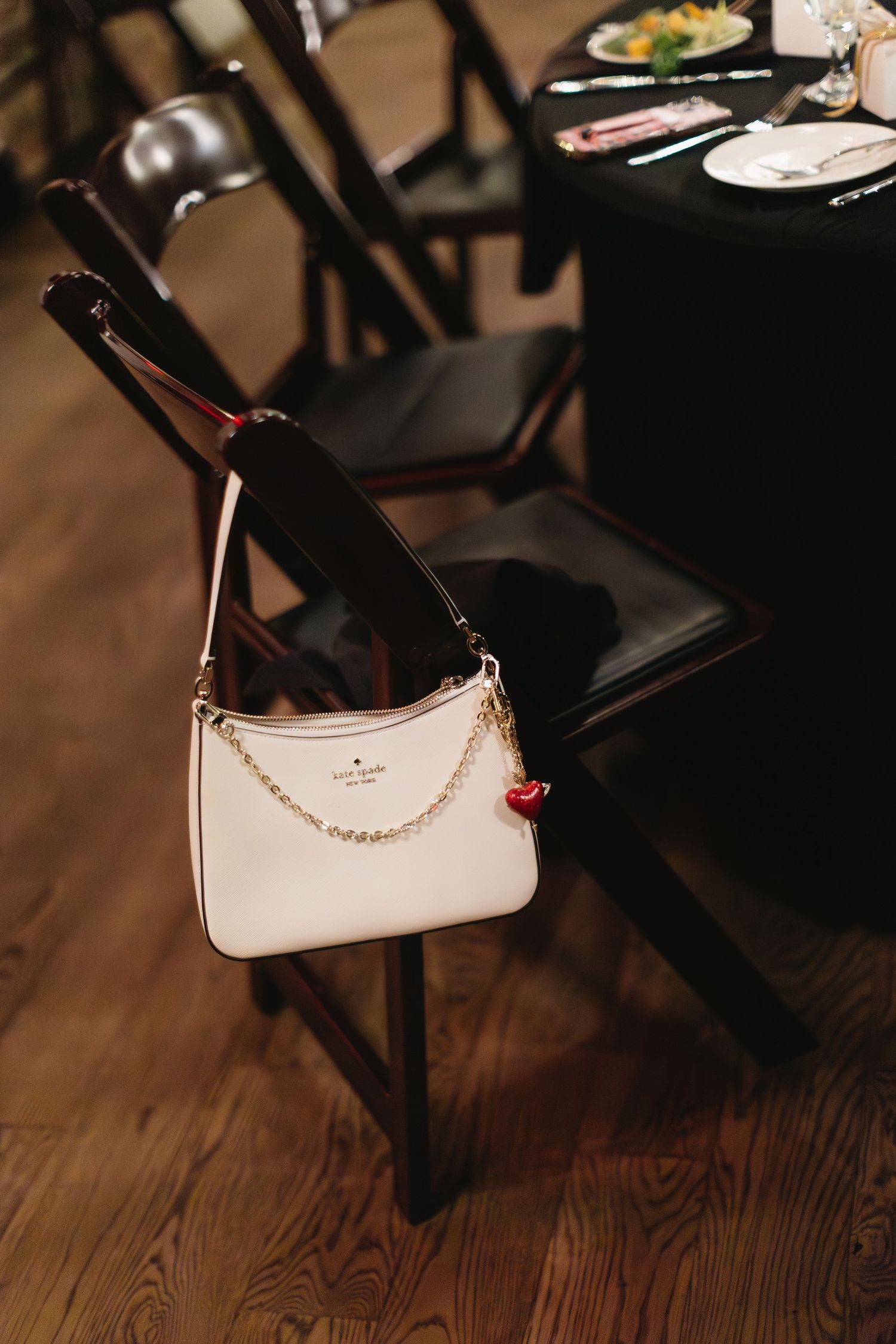 White designer handbag resting on dark wooden chairs at an event.