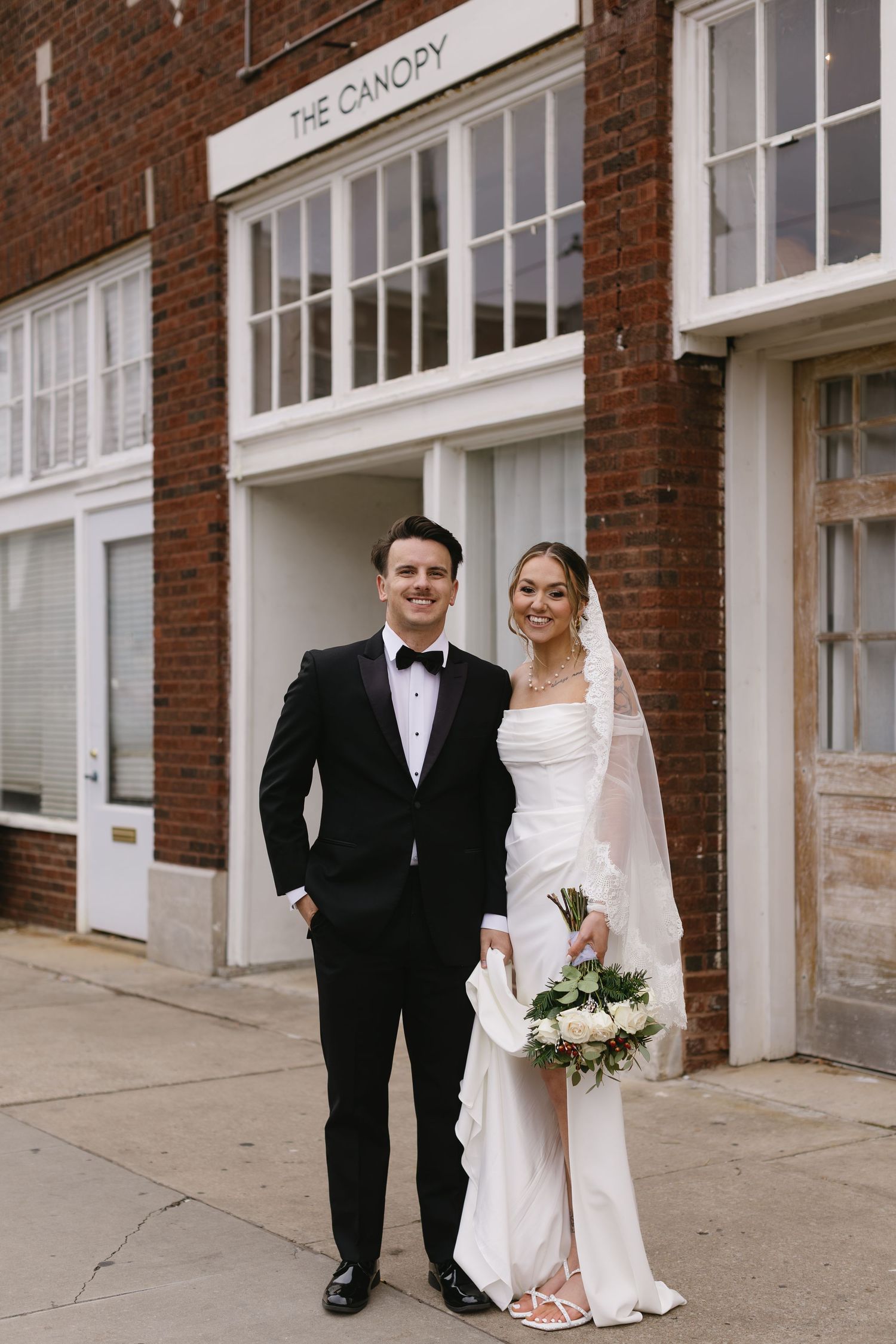 A wedding couple poses outside a brick building with 'The Canopy' signage.