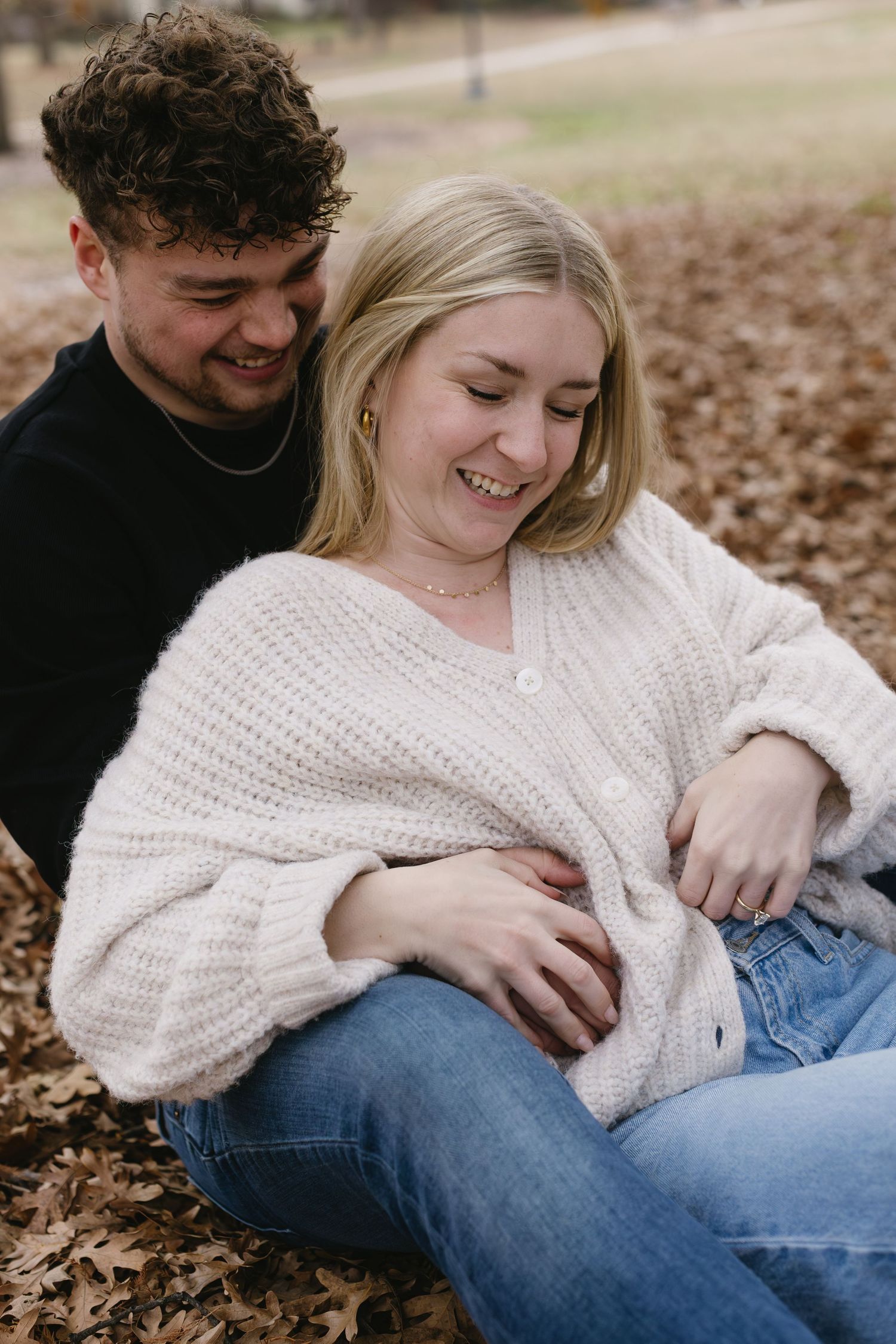 A couple lounging on autumn leaves sharing intimate moments in casual sweaters and jeans.