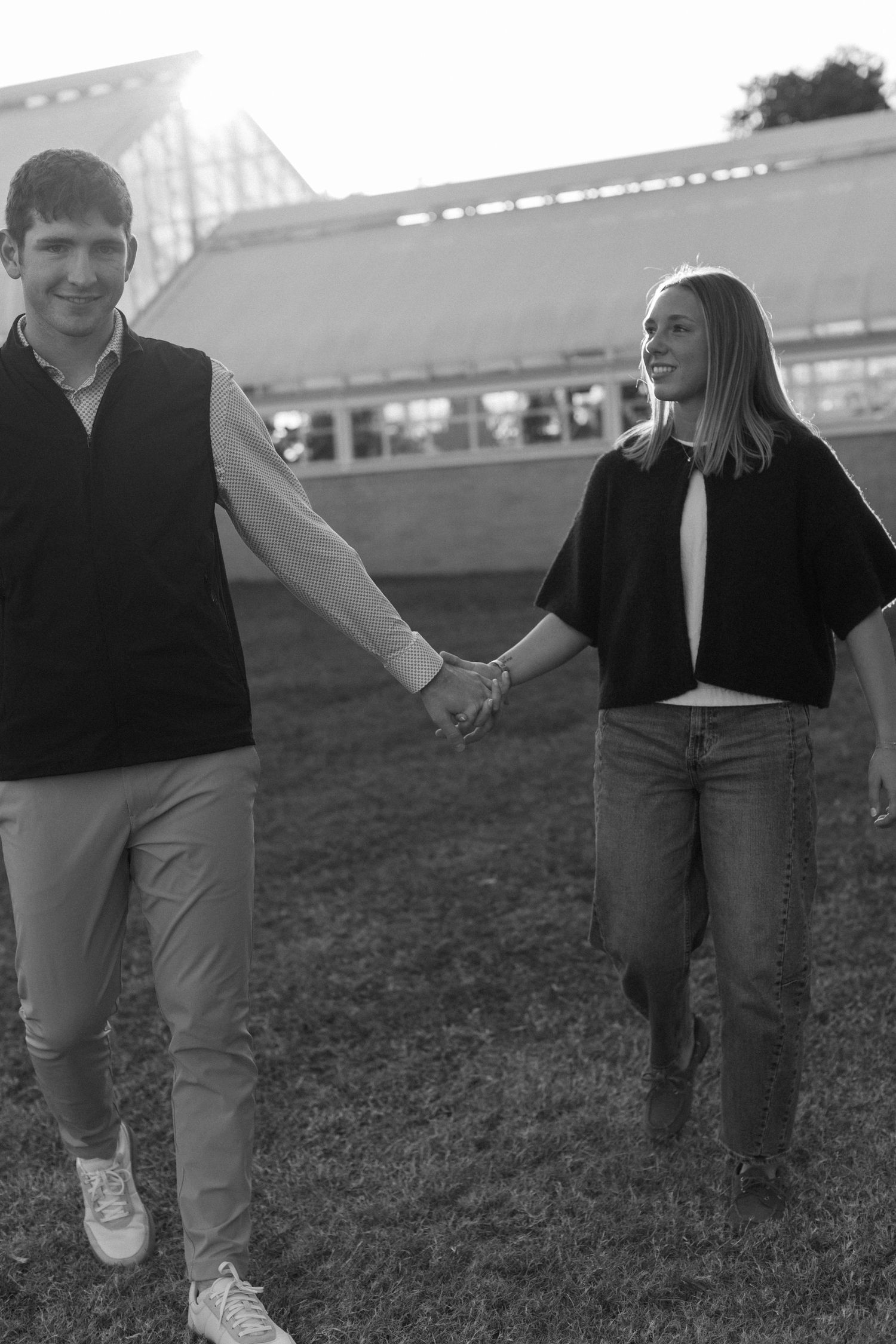 Two people playfully run together on a grassy field during sunset.